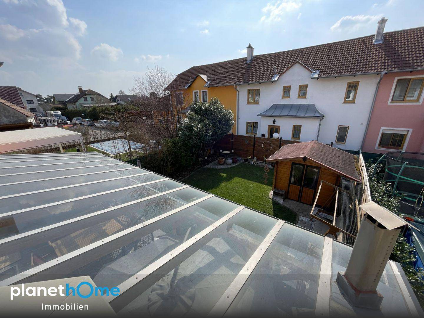 Erhöhte Ansicht des Gartens mit überdachter Terrasse, Rasenfläche und angrenzenden Reihenhäusern.