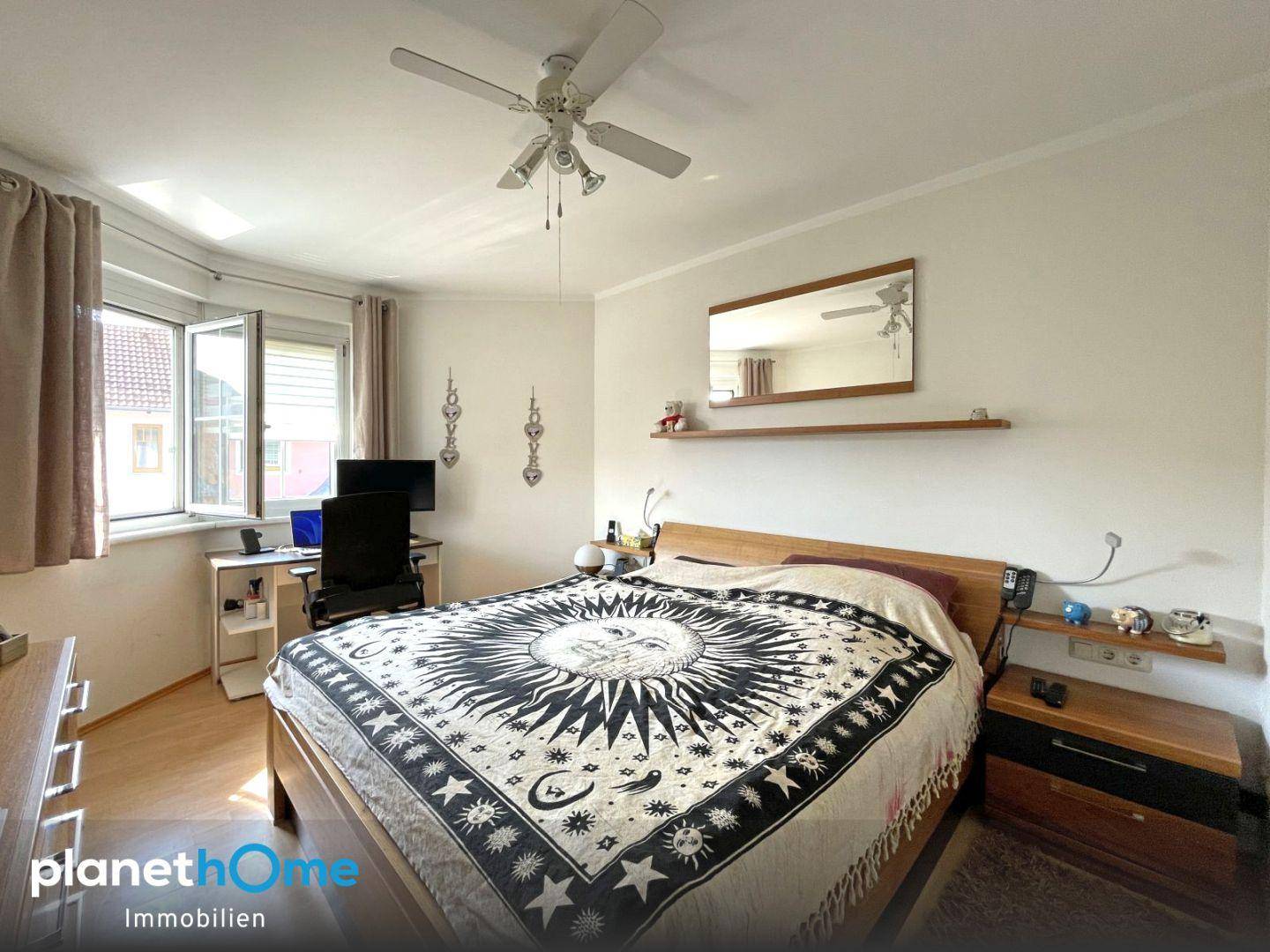 Schlafzimmer mit Doppelbett, Schreibtisch und Deckenventilator, hell und funktional eingerichtet.
