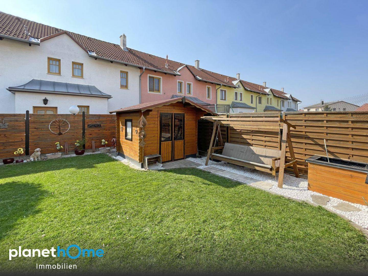 Gepflegter Hinterhof mit Rasenfläche, Gartenhaus und Holzschaukelbank, umzäunt für Privatsphäre.