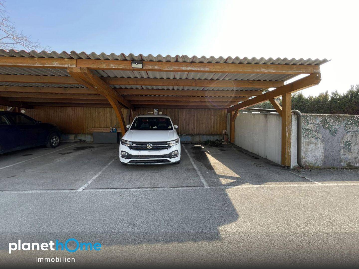 Überdachter Carport mit Holzbalkenkonstruktion bietet Schutz für Fahrzeuge vor Witterungseinflüssen.