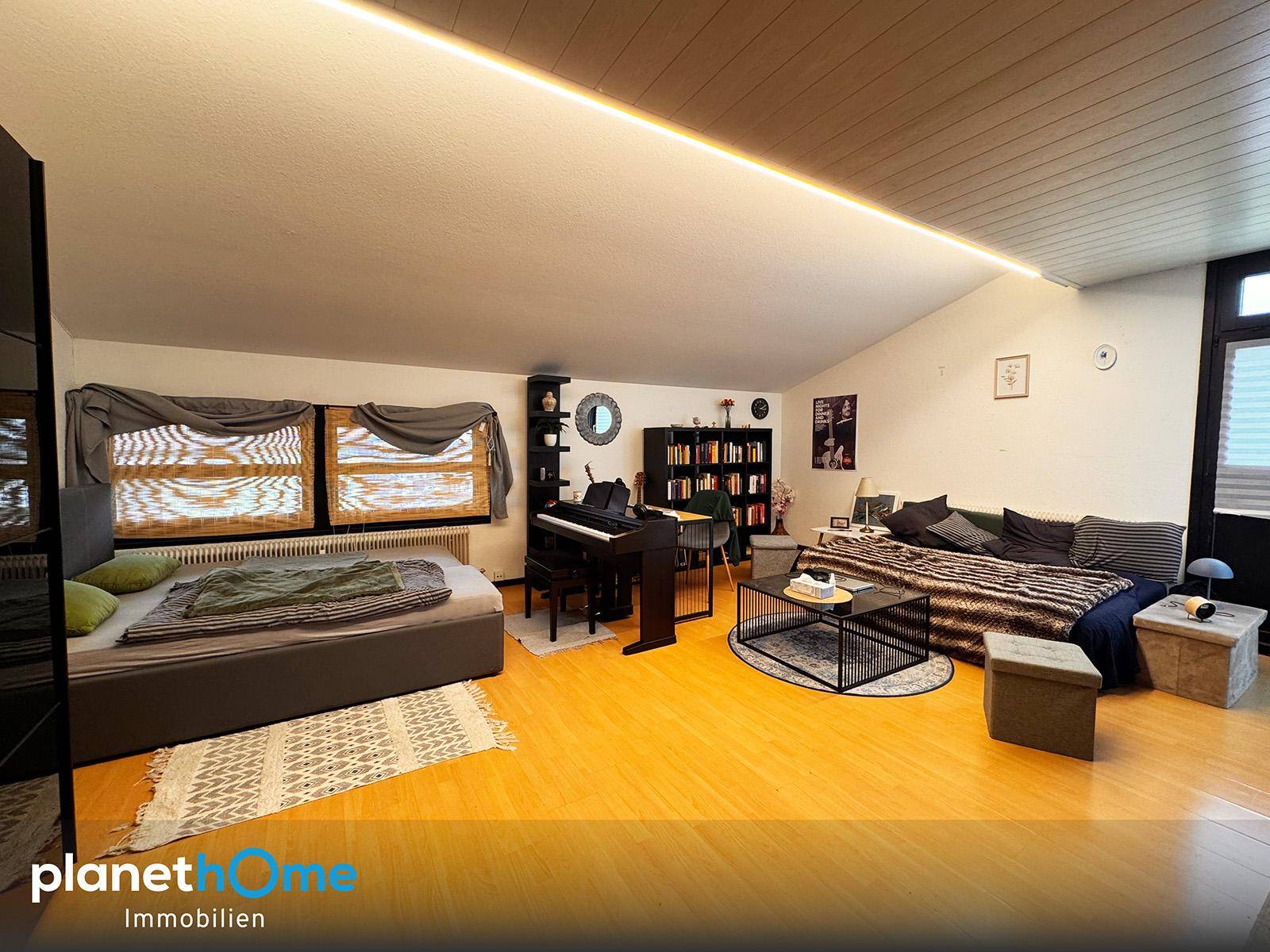 Helles Schlafzimmer mit Holzboden, Schreibtisch und gemütlicher Sitzecke unter der Dachschräge.