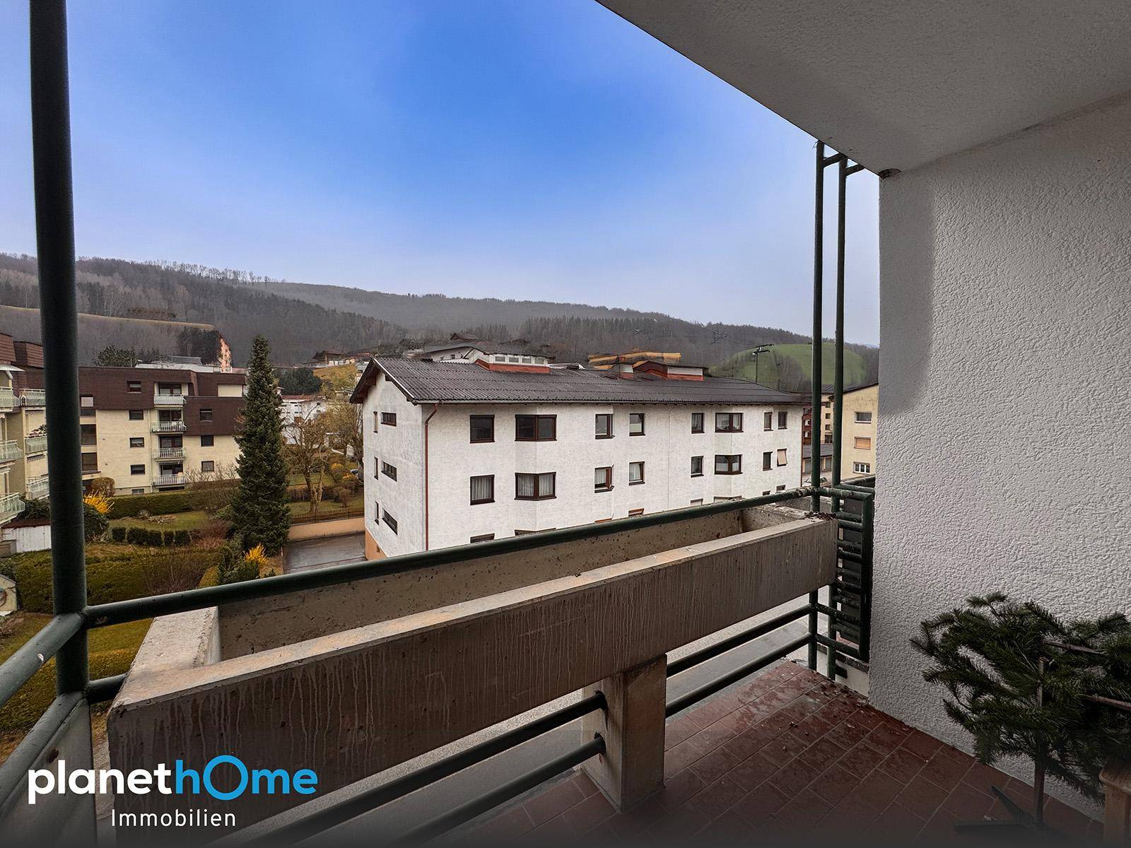 Blick vom Balkon auf die umliegenden Wohngebäude und grüne Hügellandschaft.