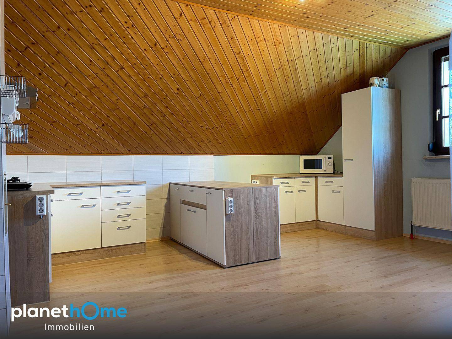 Offene Küche mit Holzdecken, Dachschrägen und einer Kücheninsel in hellem Holzdesign.