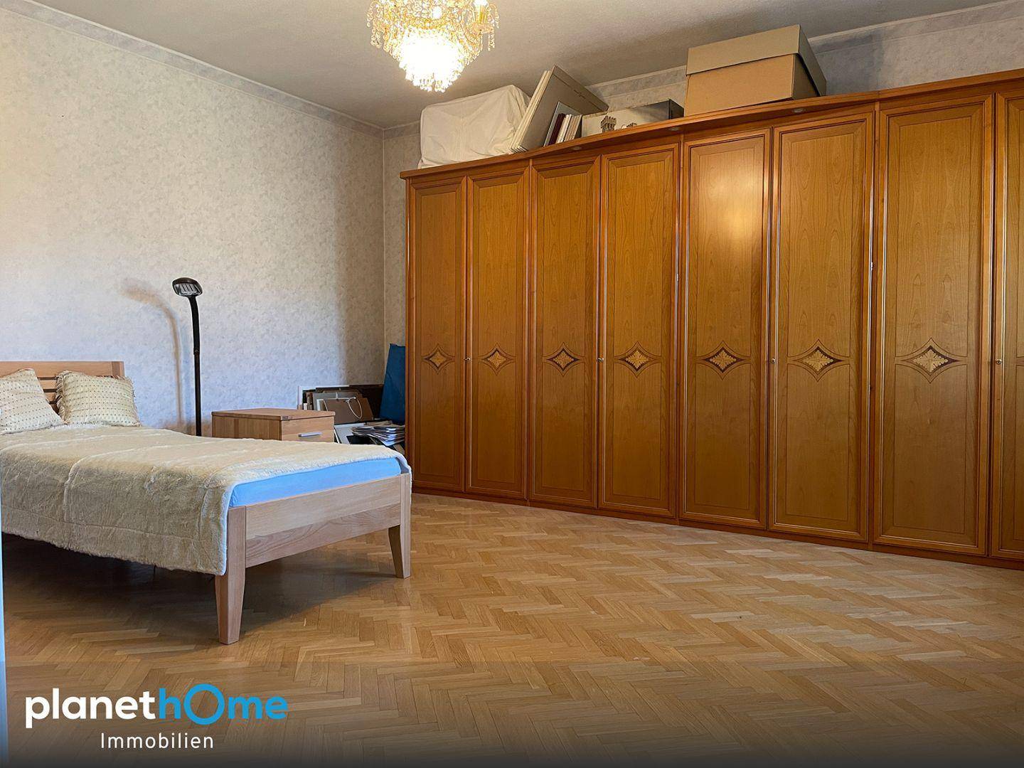 Schlafzimmer mit Parkettboden, großem Kleiderschrank und einem Doppelbett in klassischem Stil.