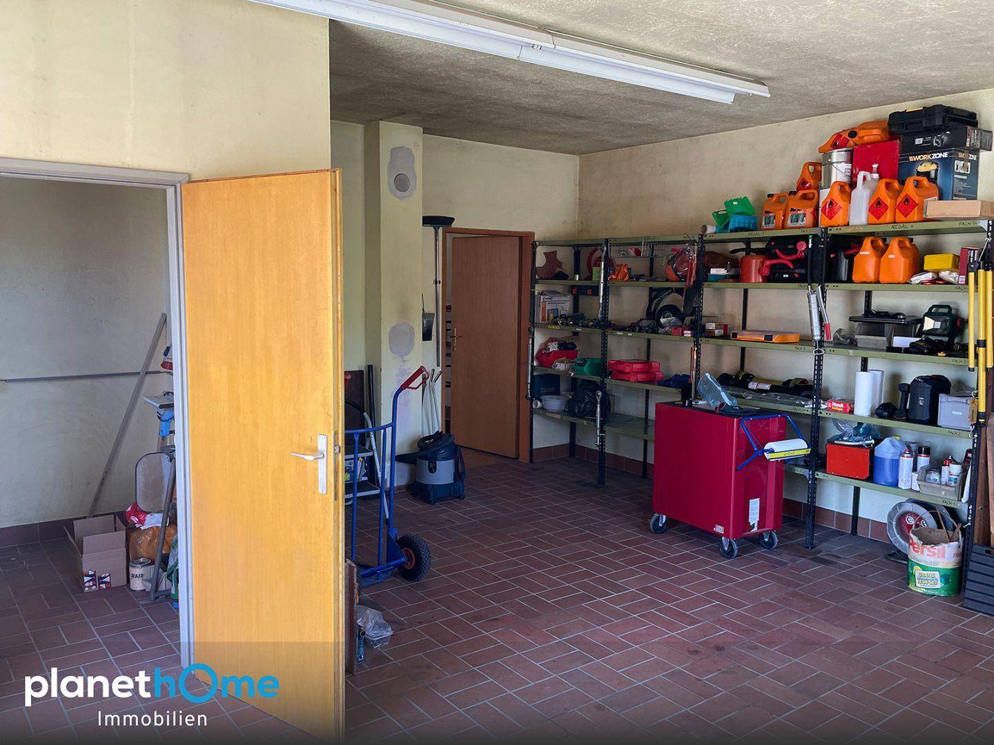 Geräumige Garage mit Fliesenboden, Regalen und verschiedenen Werkzeugen für Lagerung und Arbeit.