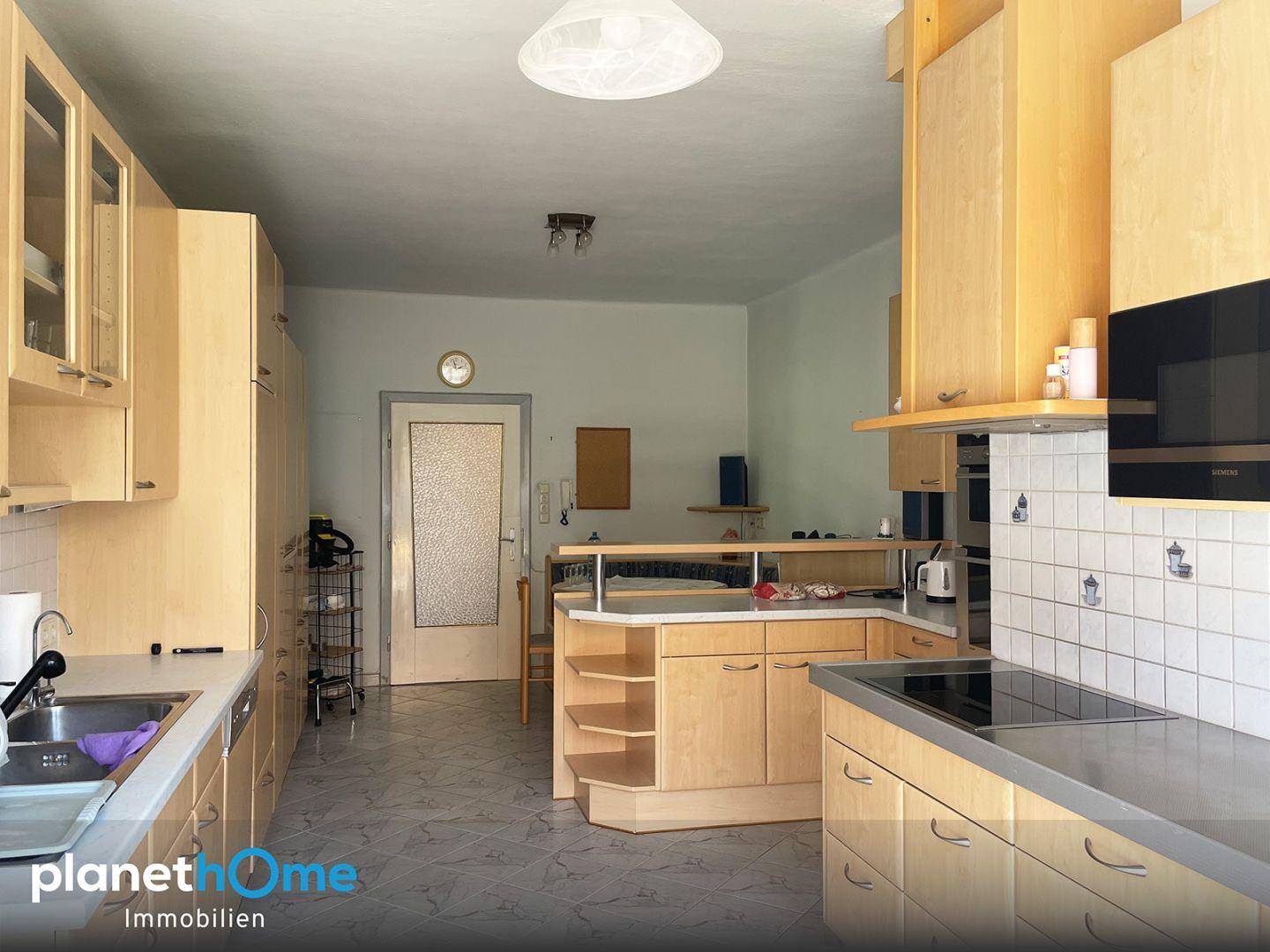 Geräumige Küche mit hellen Holzschränken, Kochinsel und Fliesenboden, ausgestattet mit modernen Geräten.