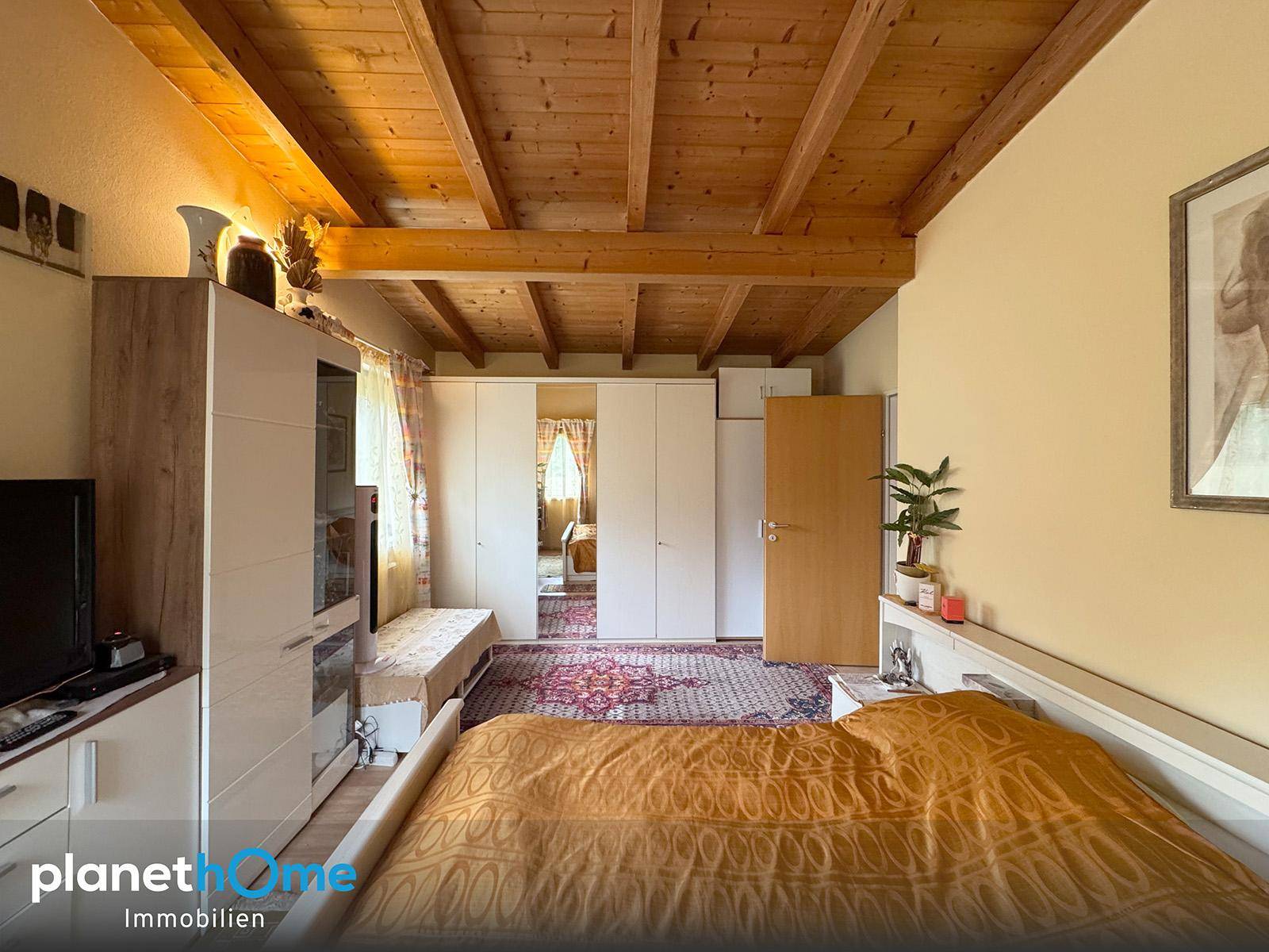 Helles Schlafzimmer mit Holzbalkendecke, Teppichboden und Blick auf den Flur.
