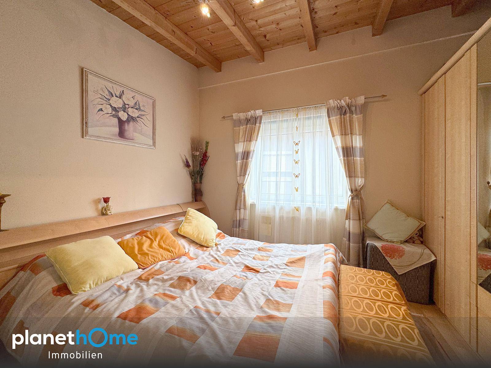 Gemütliches Schlafzimmer mit Holzbalkendecke, Doppelbett und Fenster mit karierten Vorhängen.