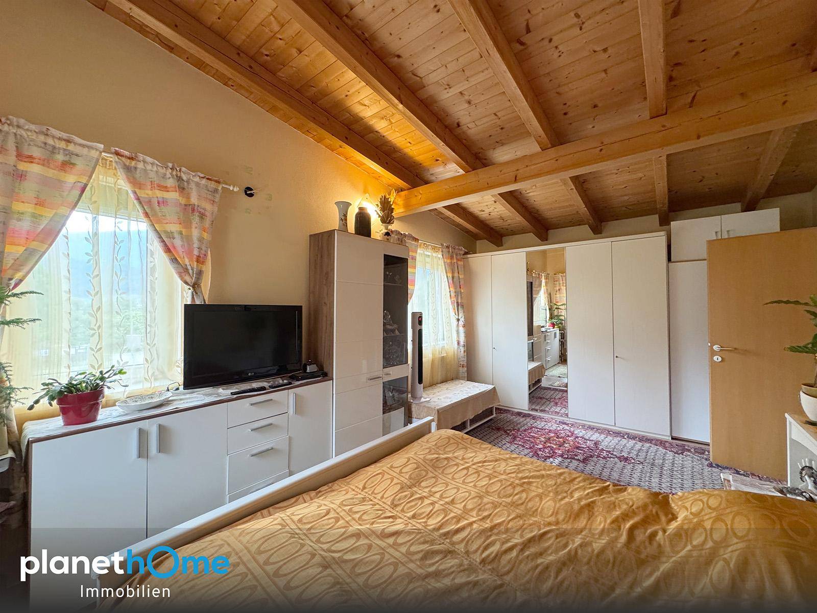 Schlafzimmer mit Holzbalkendecke, Doppelbett und weißem Kleiderschrank.
