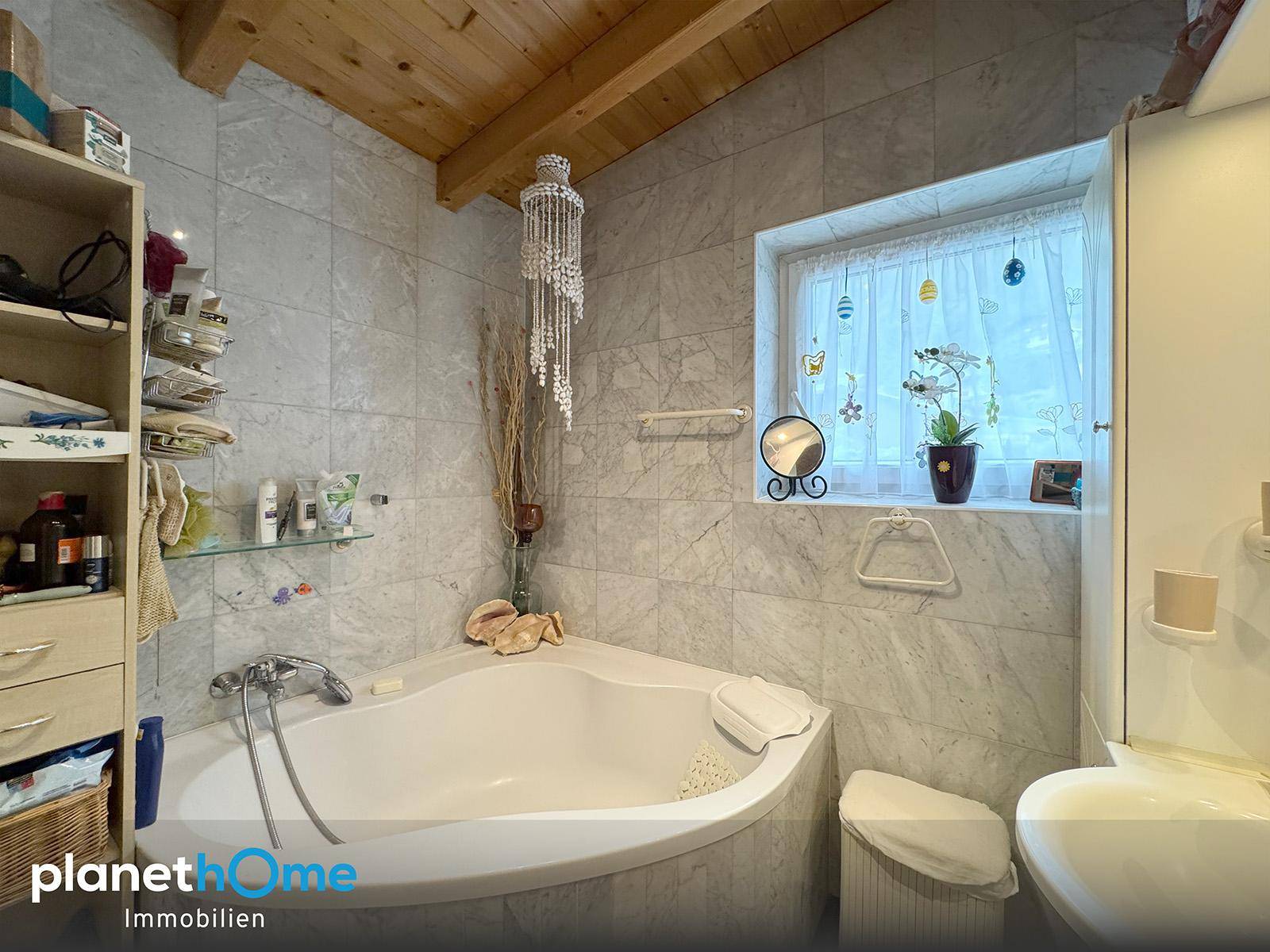 Badezimmer mit Eckbadewanne, Fliesenwänden und Holzbalkendecke.