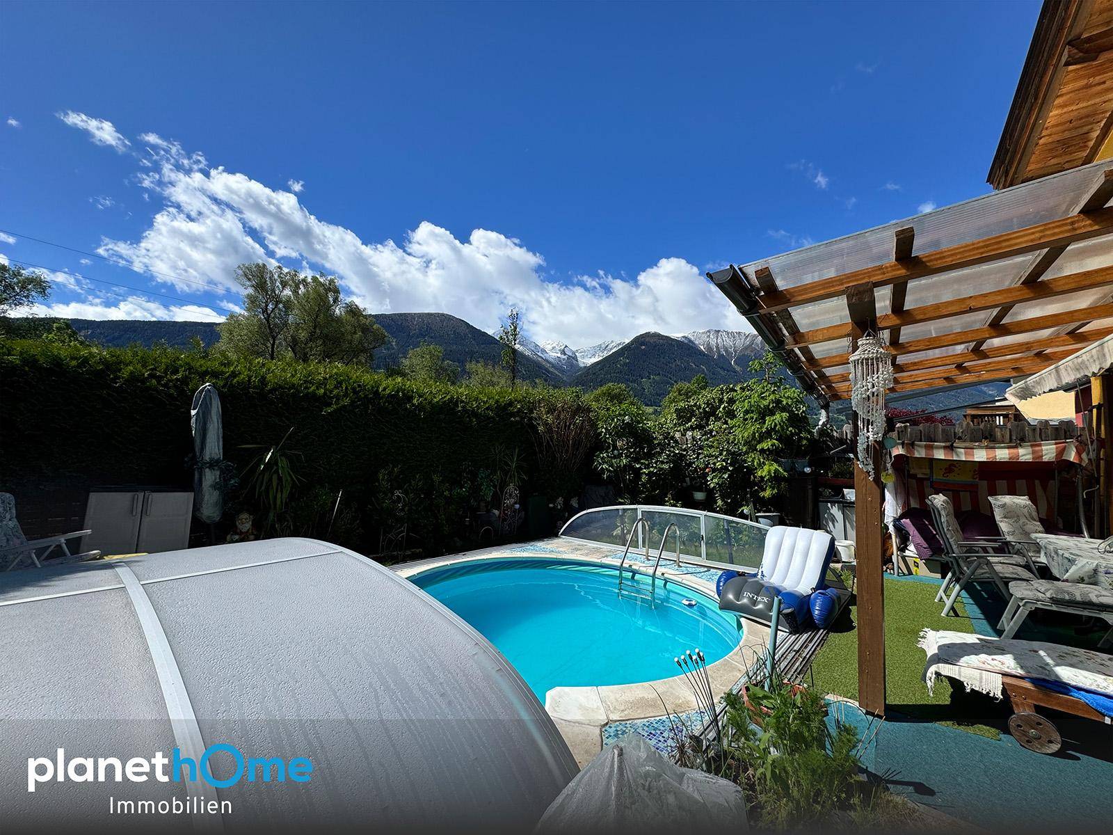 Garten mit Pool und Bergblick, umgeben von Hecken und Bäumen an einem sonnigen Tag.