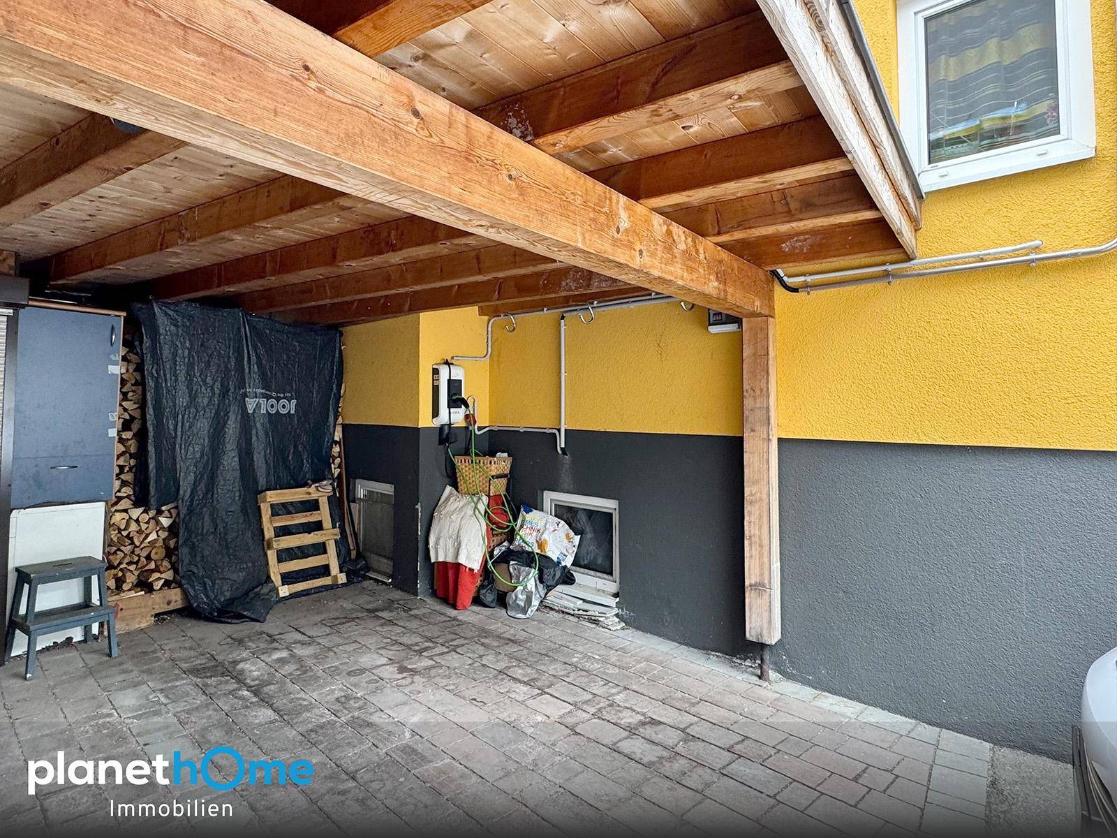 Überdachter Stellplatz oder Carport mit Holzbalken und Stauraum an der Hauswand.