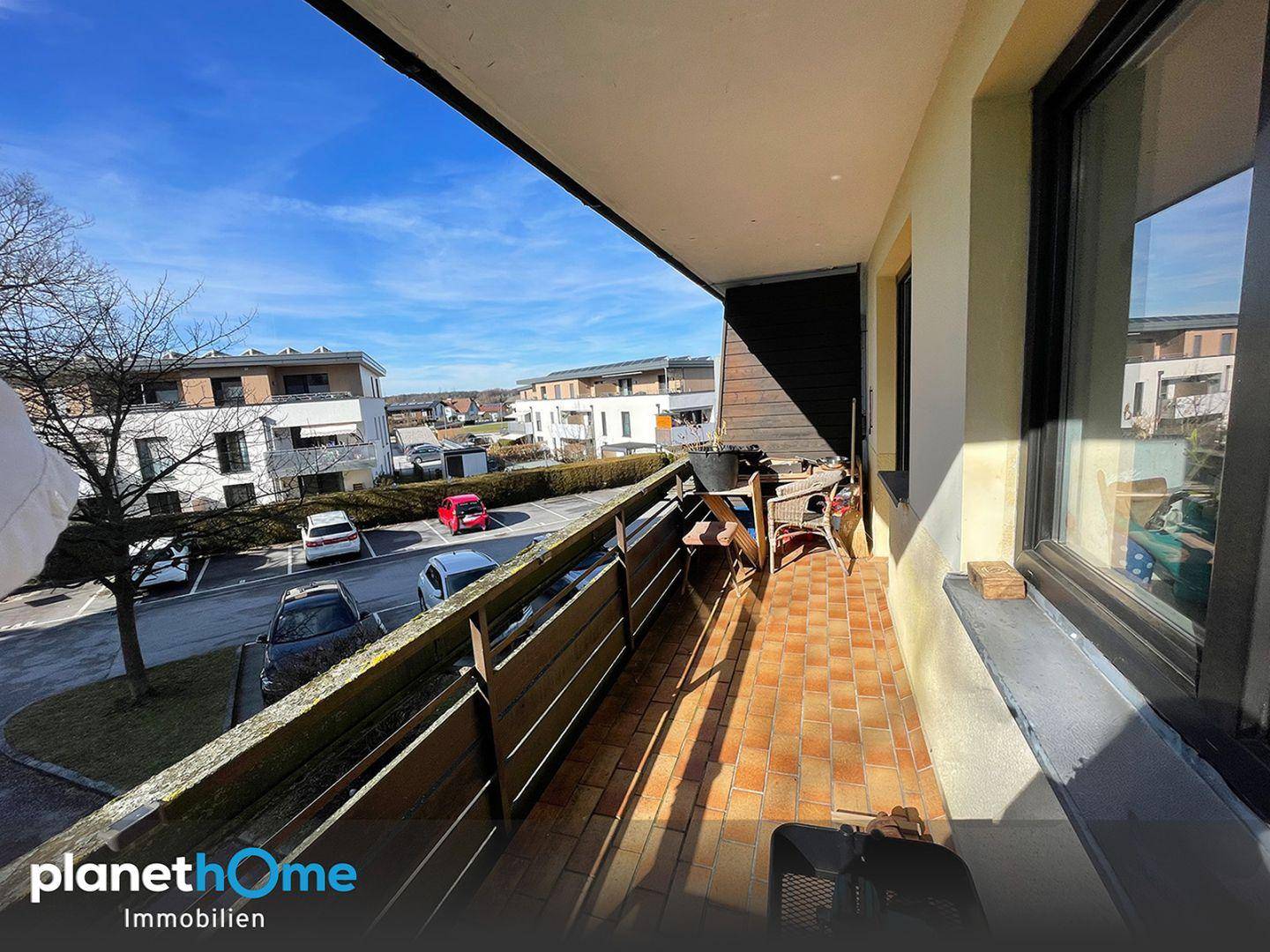 Sonniger Balkon mit Terrakotta-Fliesen, Sitzgelegenheiten und Blick auf die umliegende Wohnsiedlung.