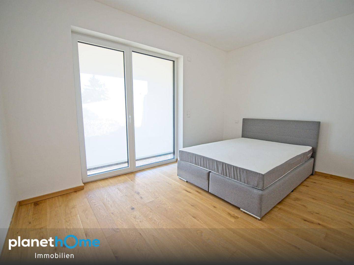 Modernes Schlafzimmer mit Holzboden und großem Fenster mit Zugang nach draußen.