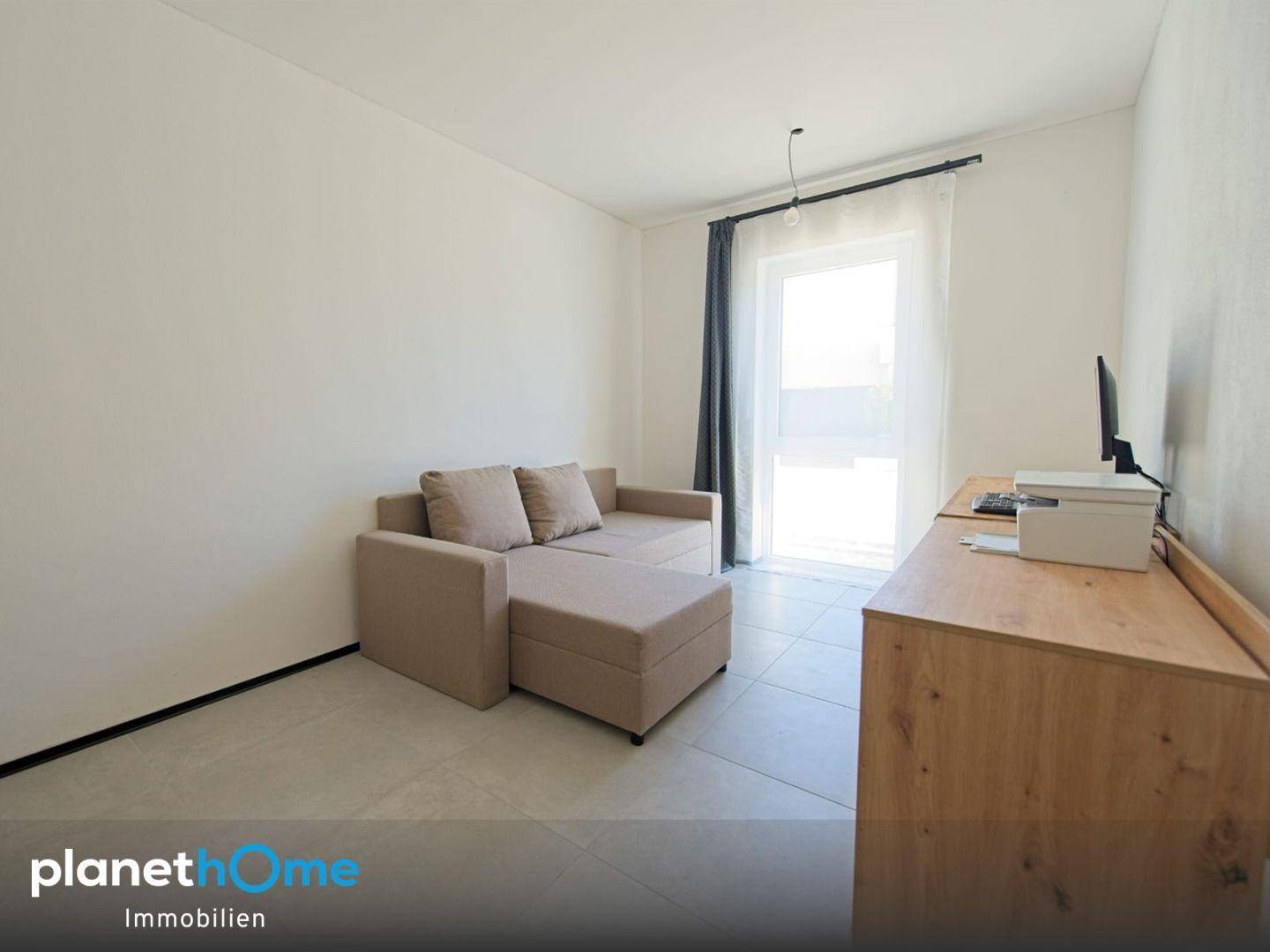 Helles Schlafzimmer mit Schlafsofa, Fliesenboden und Fenster mit Vorhängen.