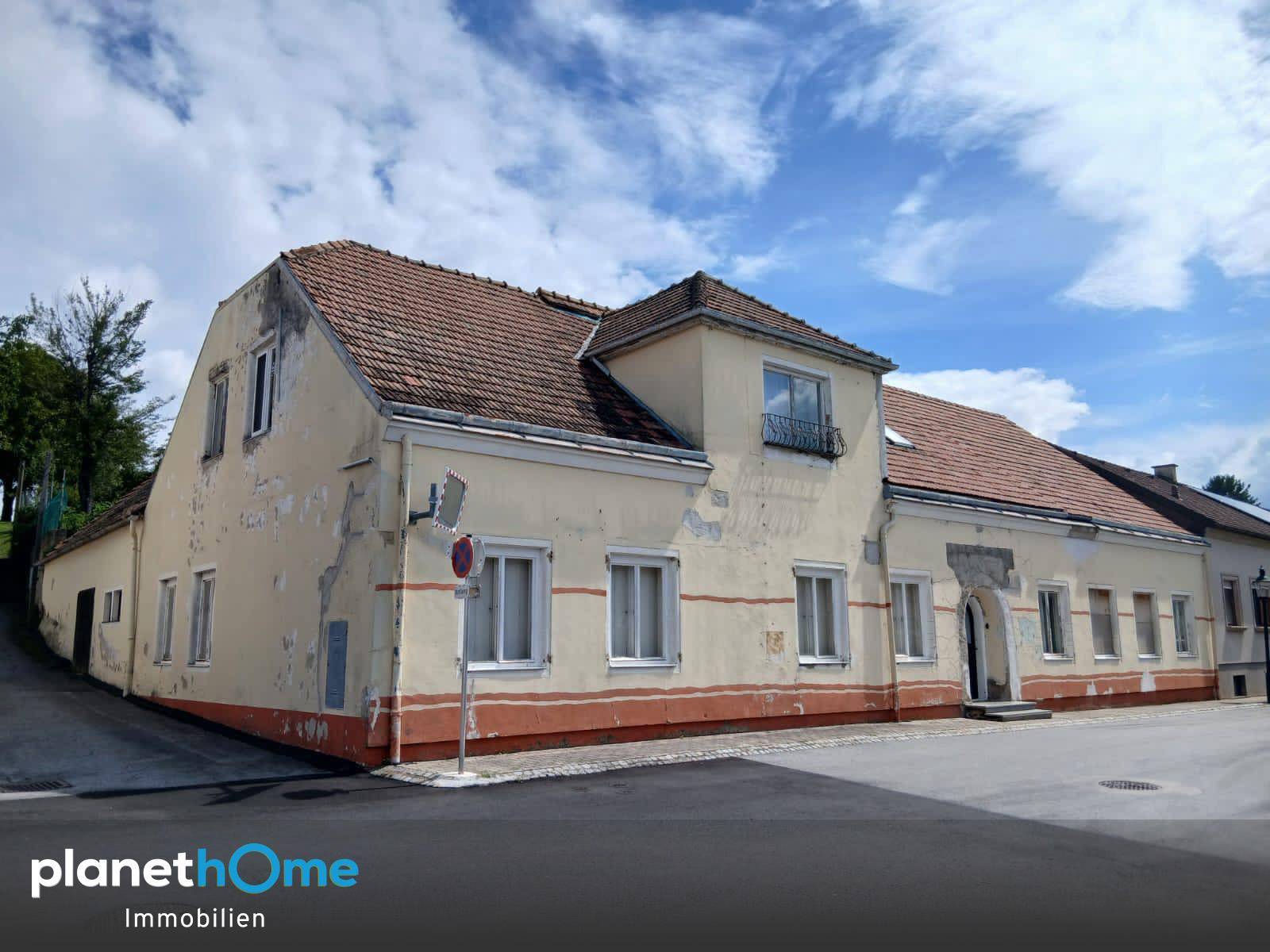 Altes Gebäude mit verputzter Fassade und Ziegeldach, das Renovierungsbedarf aufweist.