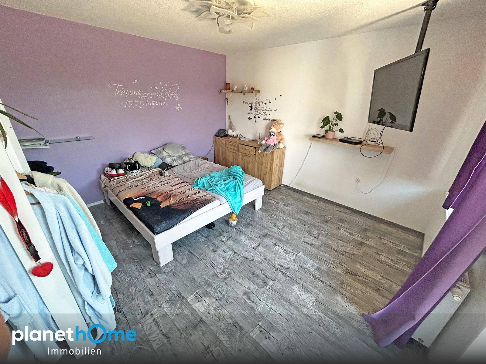 Schlafzimmer mit lila Wand, Holzboden und Fernseher an der Wand.
