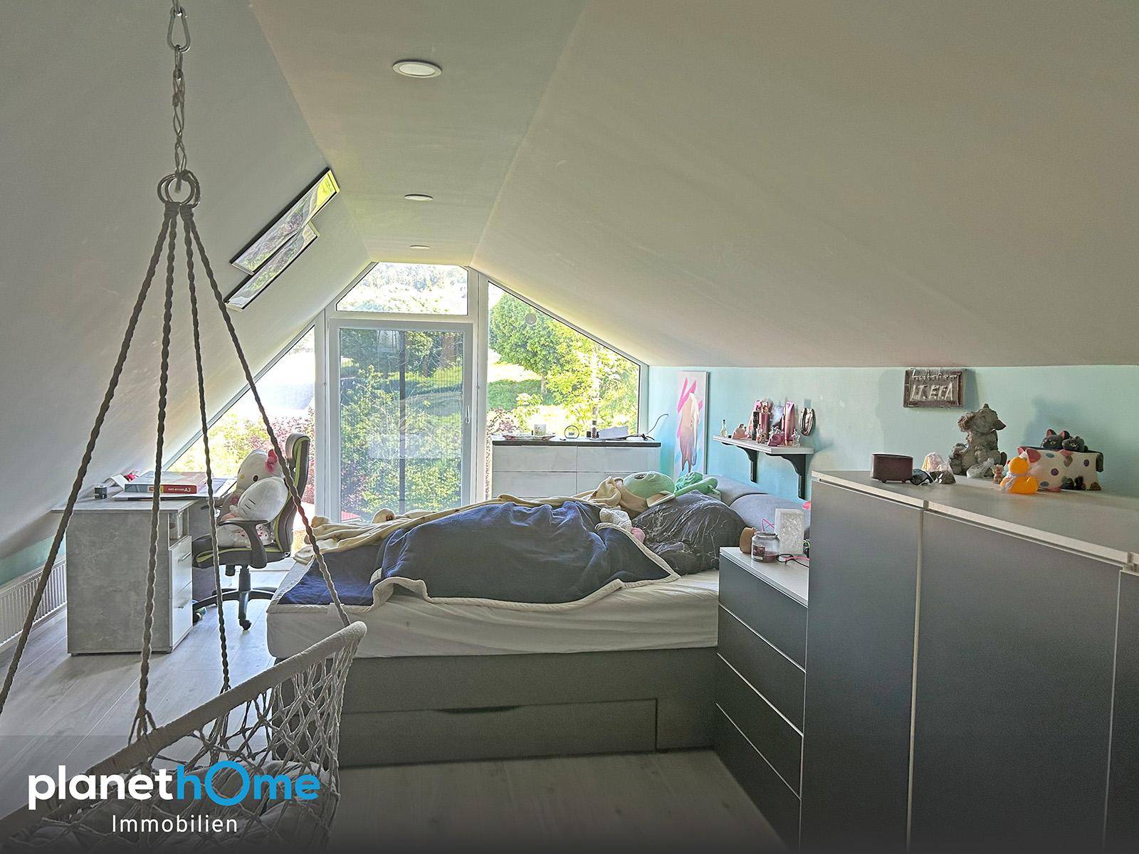 Gemütliches Schlafzimmer im Dachgeschoss mit großen Fenstern und Schaukelstuhl.