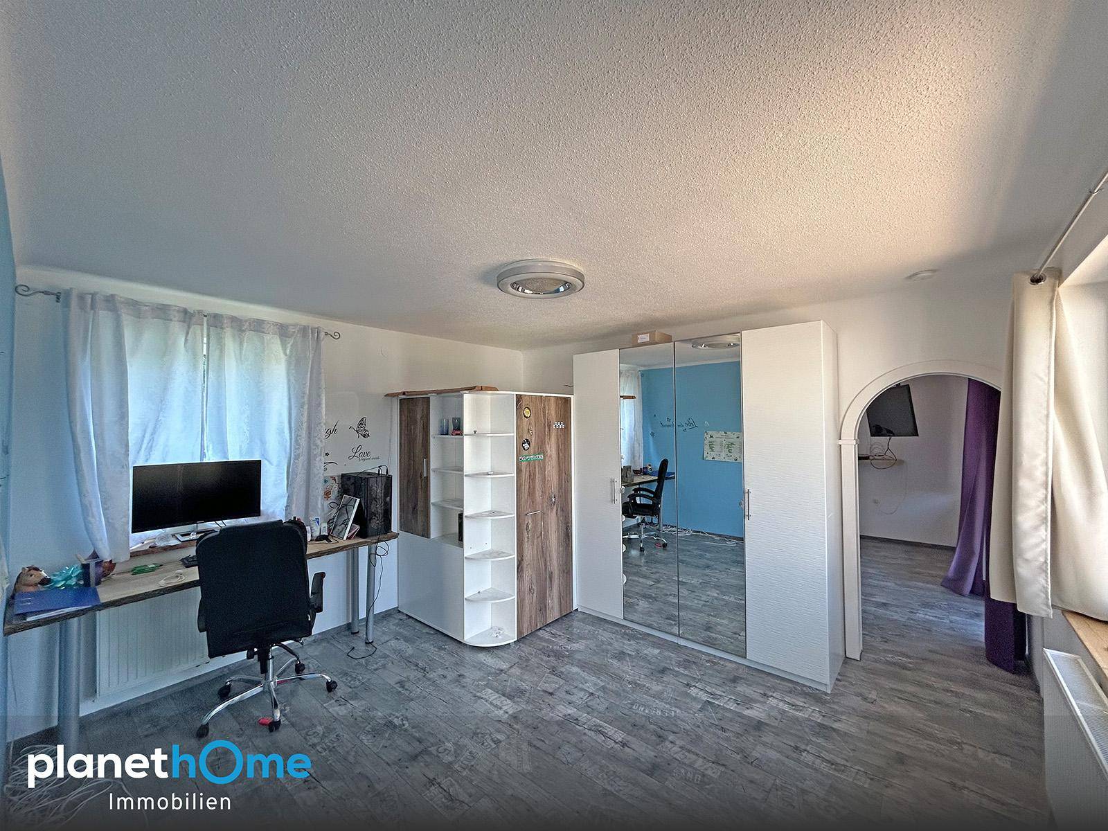 Helles Arbeitszimmer mit Schreibtisch, Spiegelschrank und Blick ins Grüne.