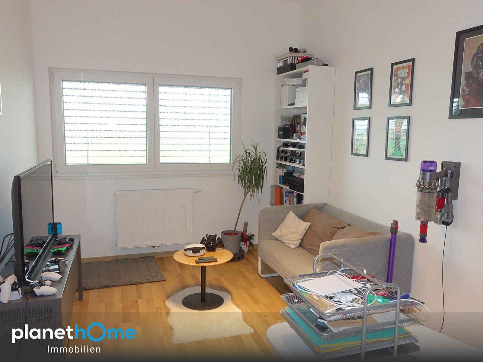 Gemütliches Wohnzimmer mit Sofa, Fernseher und einem großen Fenster, das viel Licht hereinlässt.