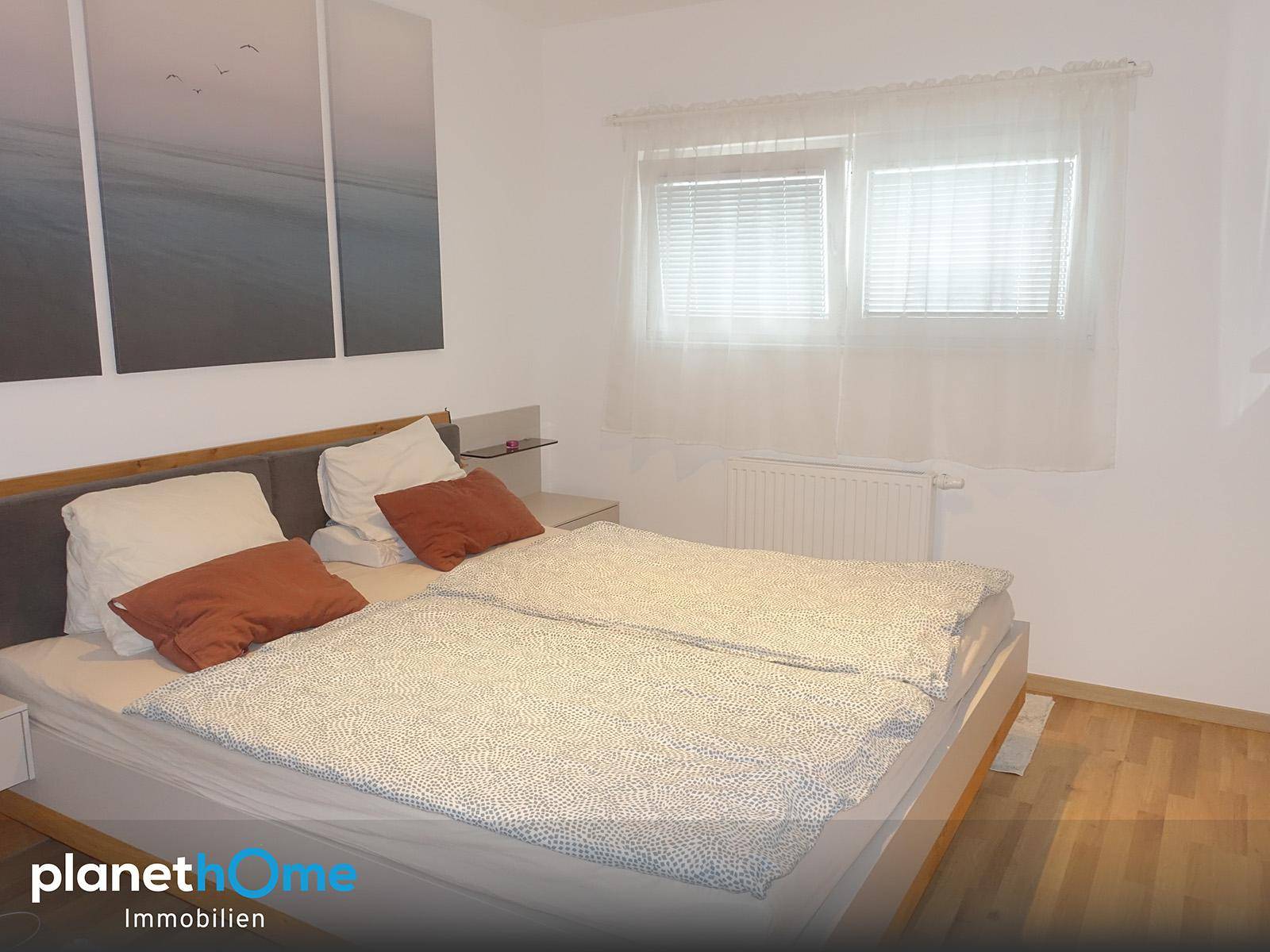Weiteres Schlafzimmer mit Doppelbett, hellem Holzfußboden und einem Fenster mit Vorhängen.
