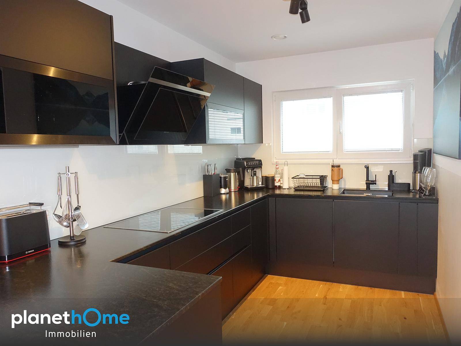 Moderne schwarze Einbauküche mit dunklen Arbeitsplatten, Induktionskochfeld und Fenster.