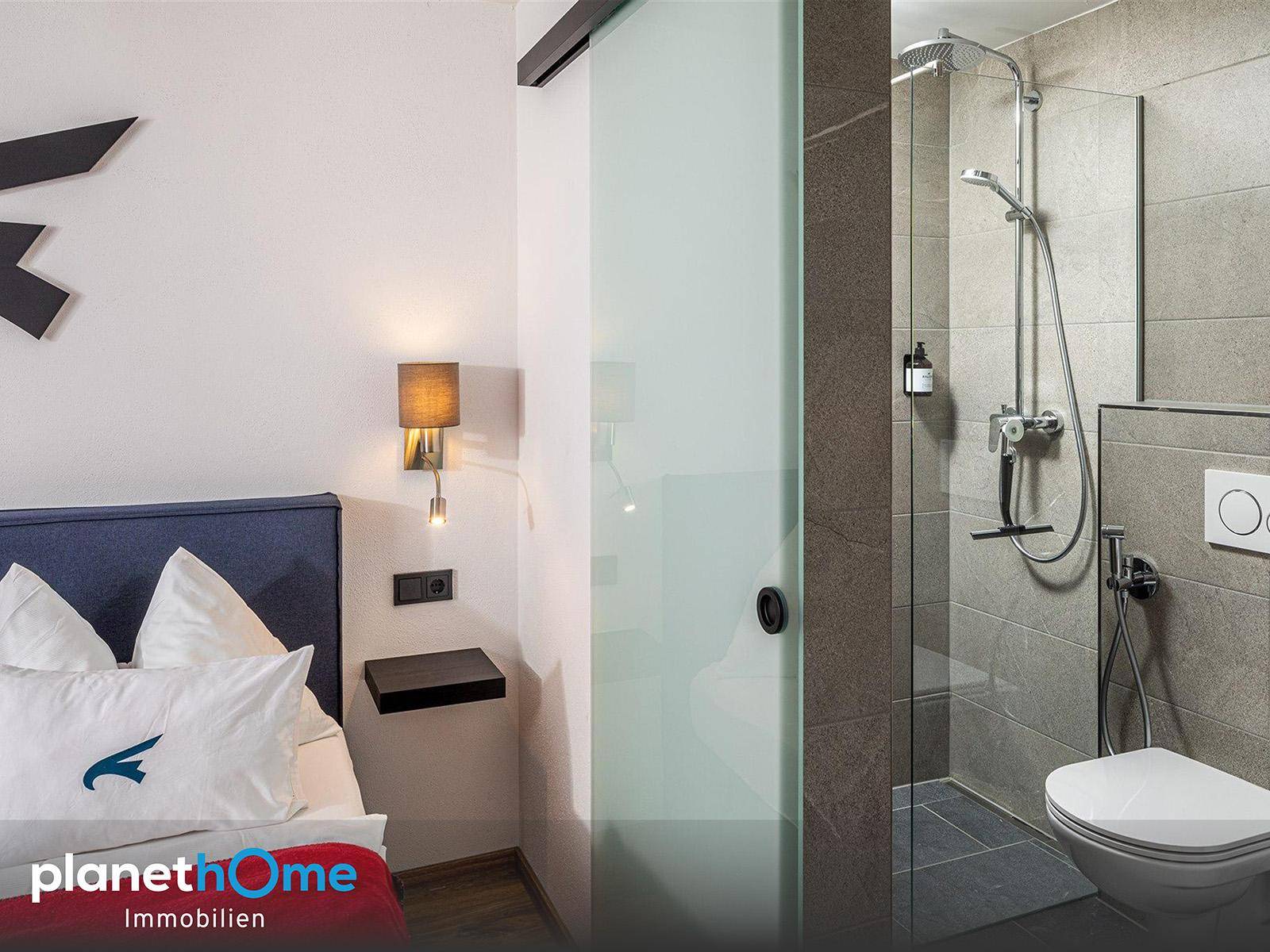 Schlafzimmer mit Zugang zu einem modernen Badezimmer, ausgestattet mit Dusche und Toilette, durch eine Glasschiebetür.