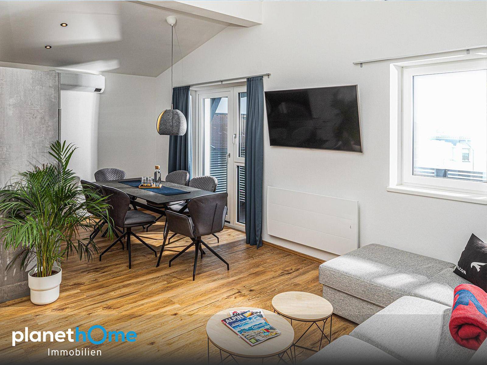 Heller Wohn- und Essbereich mit Holzboden, Esstisch, Sofa und großem Wandfernseher, modern eingerichtet.