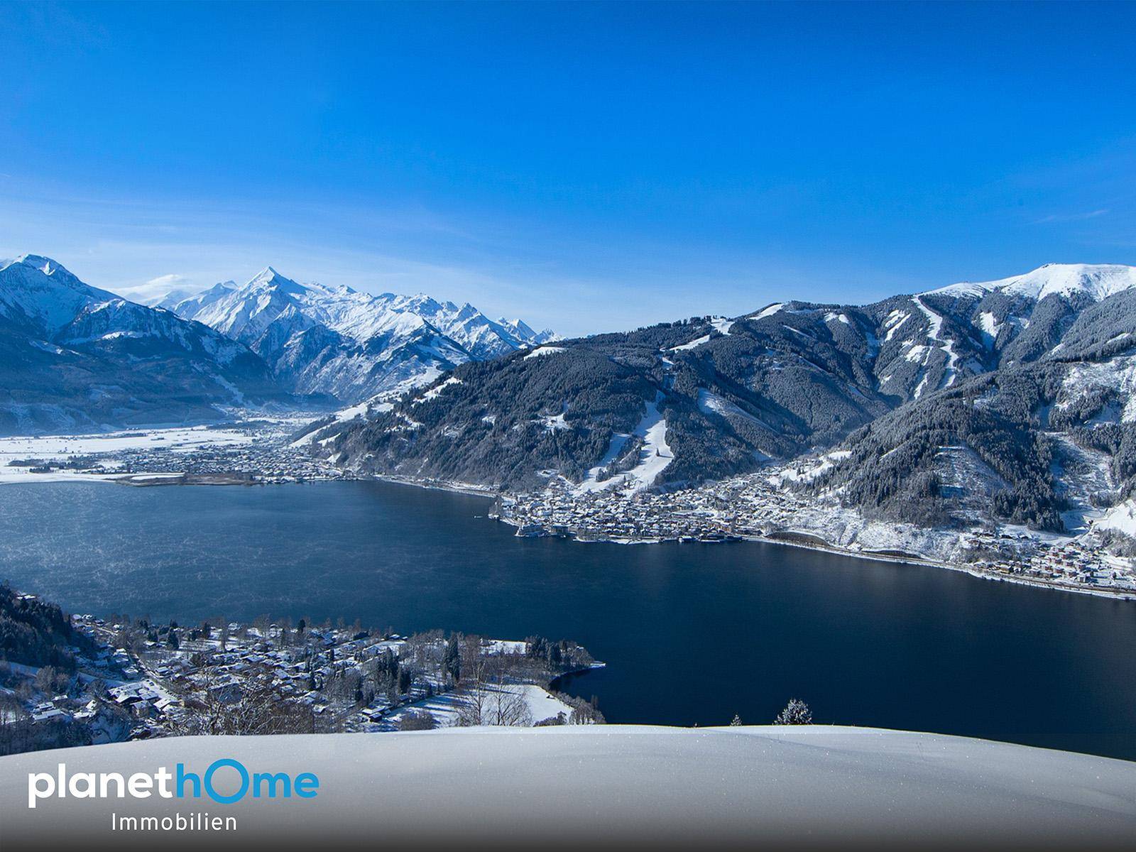 Atemberaubender Winterblick auf einen zugefrorenen See, umgeben von schneebedeckten Bergen und einer Stadt.
