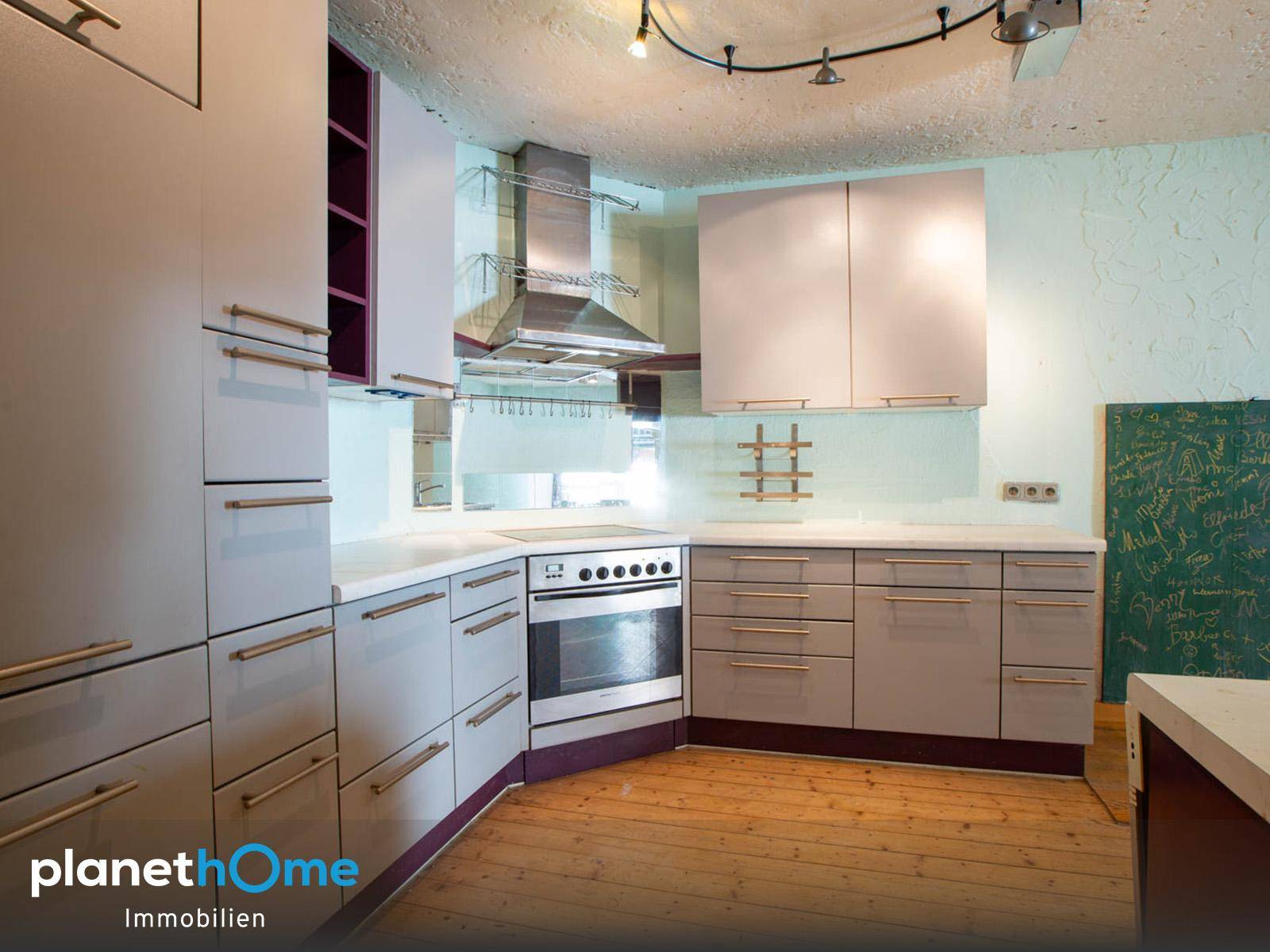 Moderne Küche mit grauen Schränken, Backofen, Induktionskochfeld und Holzdielenboden.