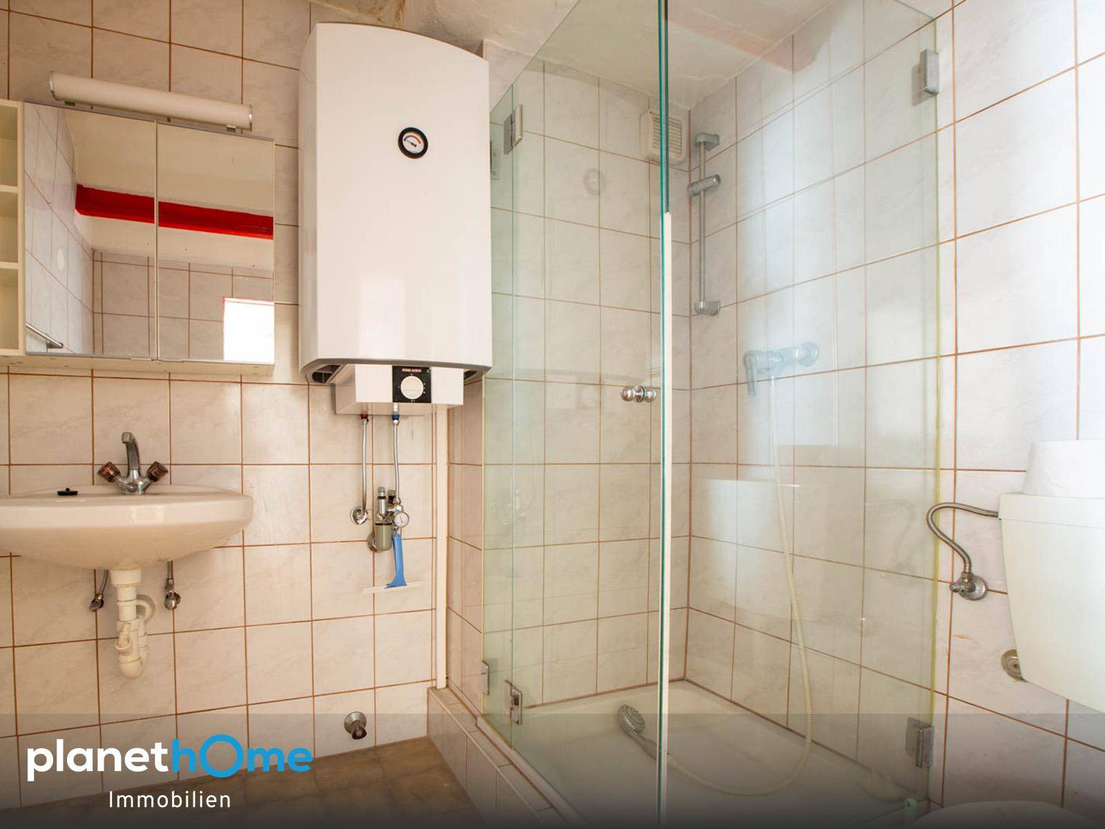 Funktionales Badezimmer mit Duschkabine, Waschbecken und Warmwasserboiler.
