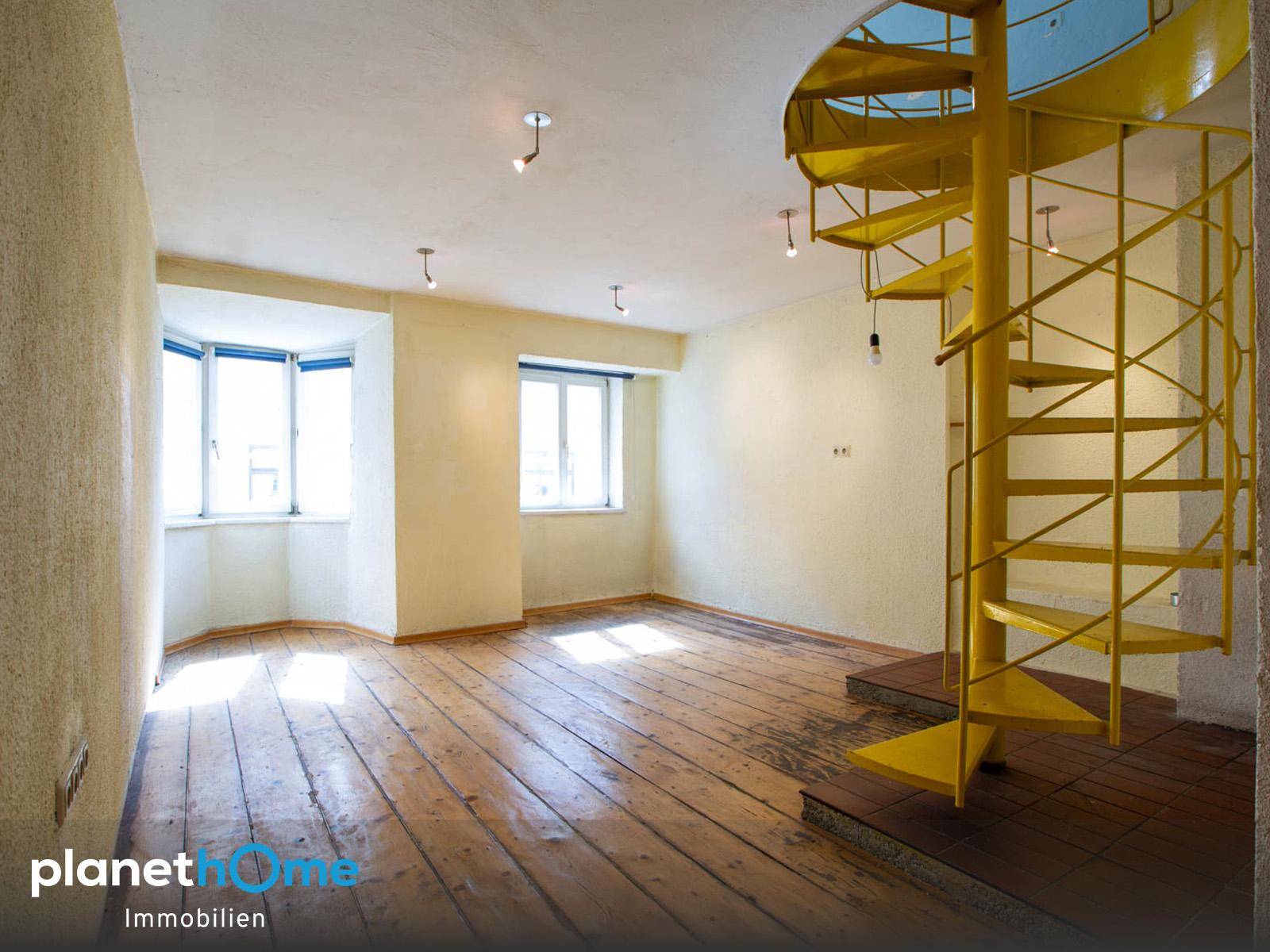 Heller Raum mit Dielenboden, Erkerfenster und einer auffälligen gelben Wendeltreppe.