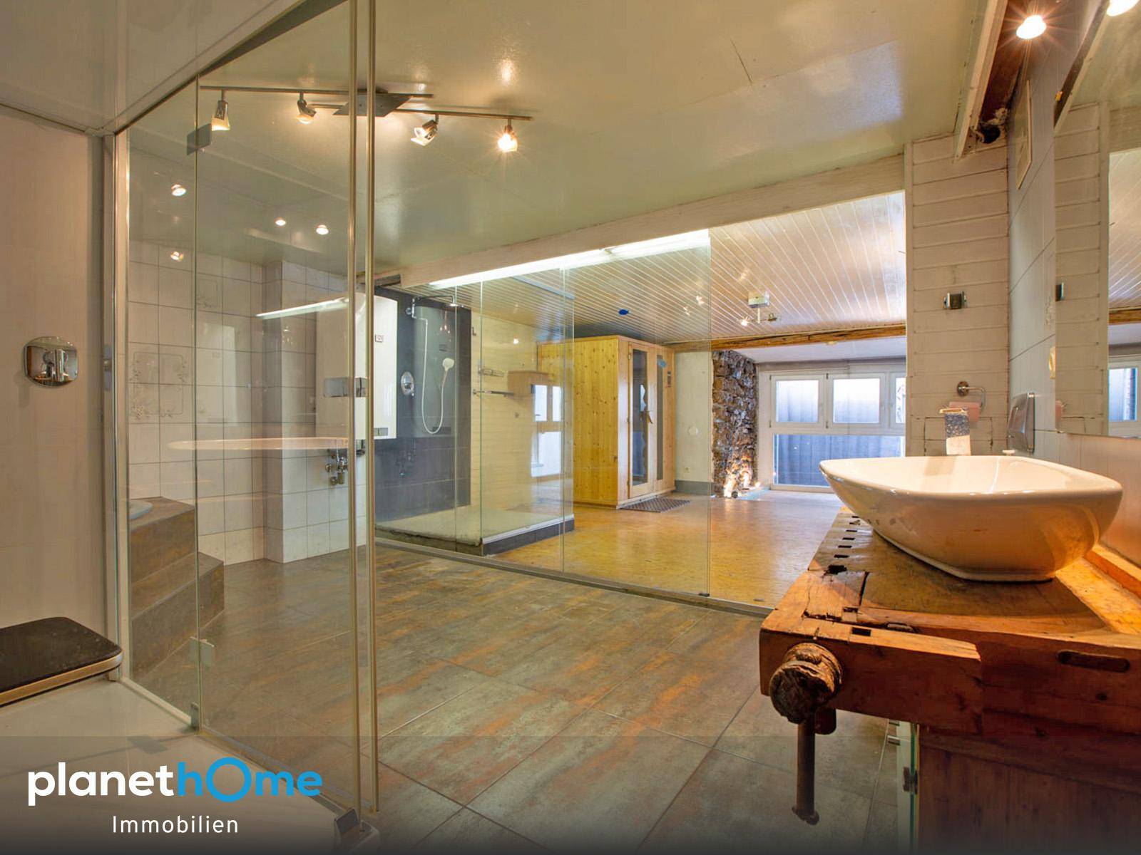 Exklusiver Wellnessbereich mit großer Glasdusche, Sauna und modernem Waschbecken.
