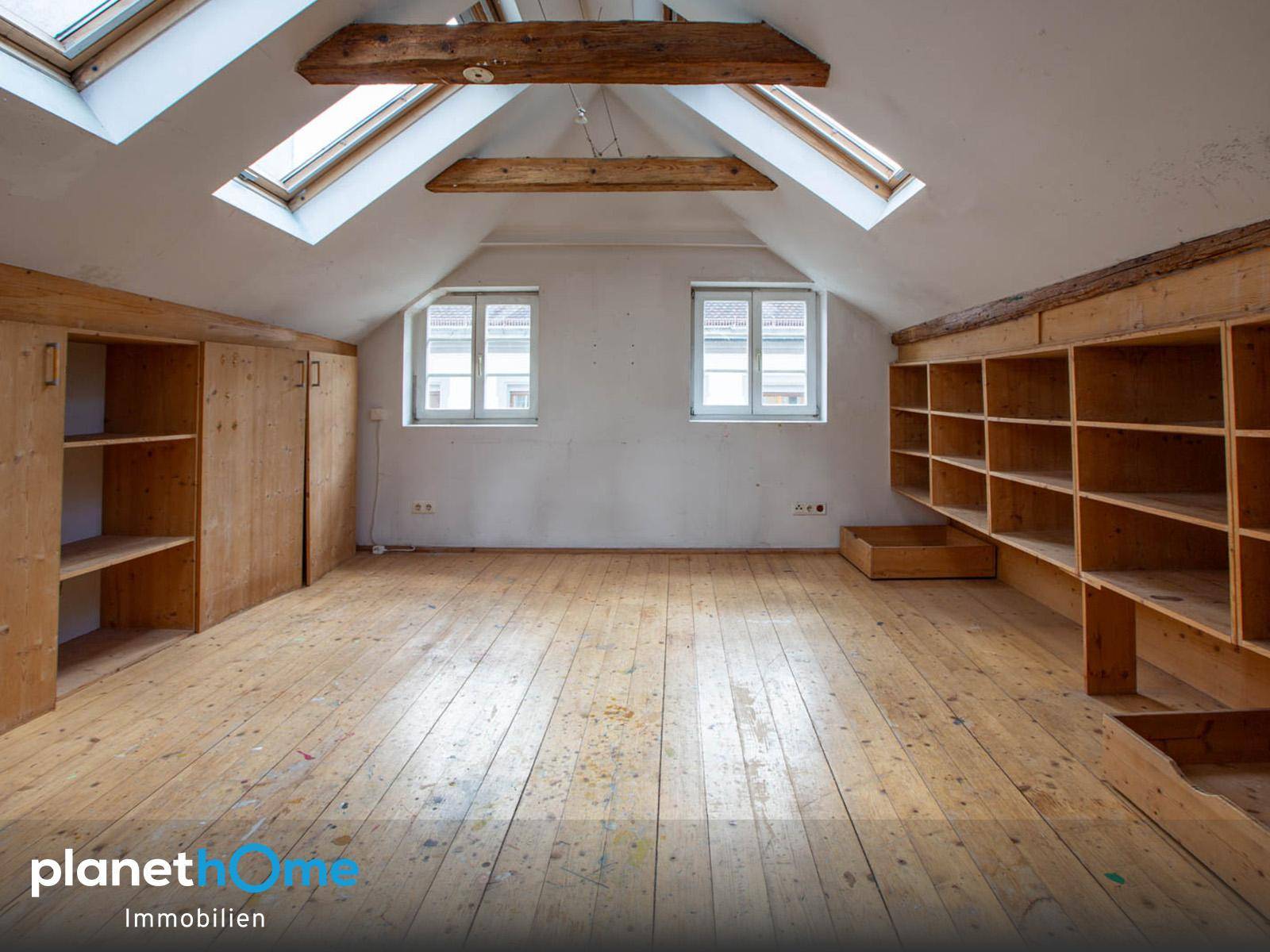 Helles Dachgeschosszimmer mit sichtbaren Holzbalken, Dachfenstern und Einbauregalen.