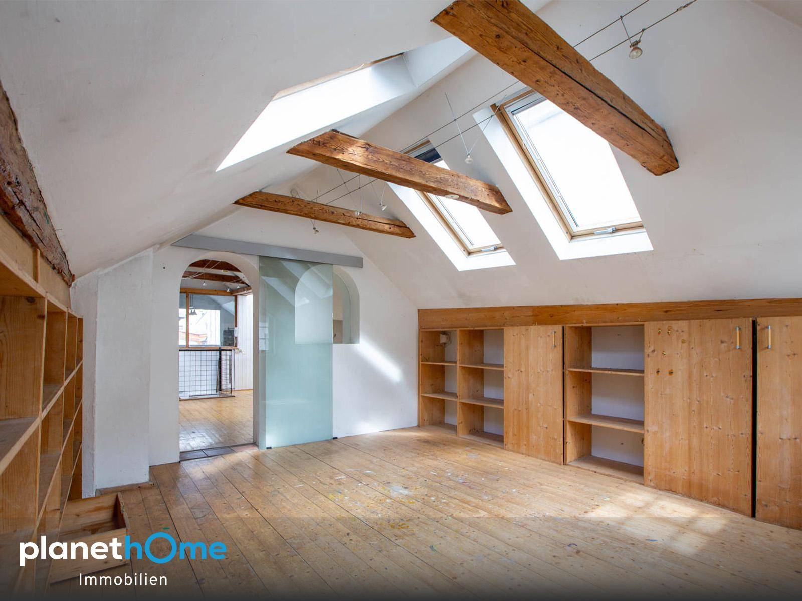 Helles Dachgeschosszimmer mit sichtbaren Holzbalken, Dachfenstern und Einbauregalen.