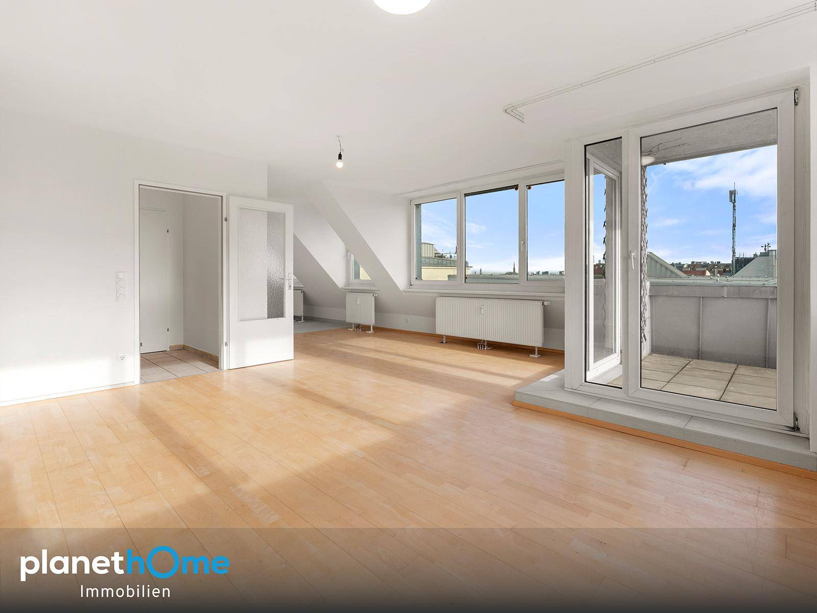 Geräumiger, heller Raum mit Holzboden, Dachschräge und direktem Zugang zu einem Balkon.