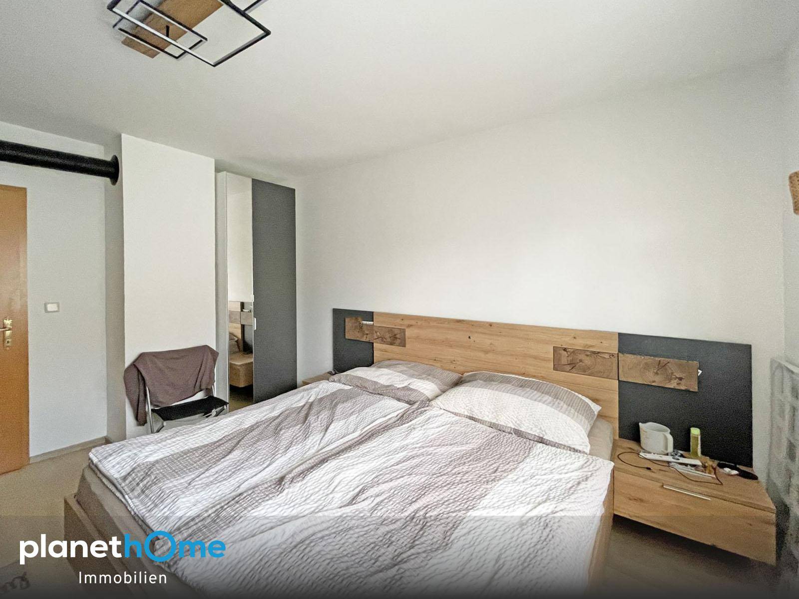 Schlafzimmer mit Doppelbett, Holzkopfteil und schlichten weißen Wänden.