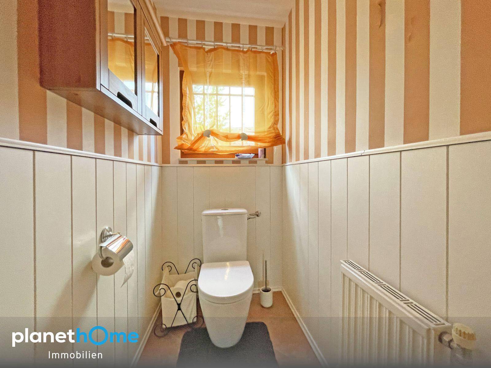 Separate Toilette mit gestreiften Tapeten, Holzvertäfelung und Fenster.