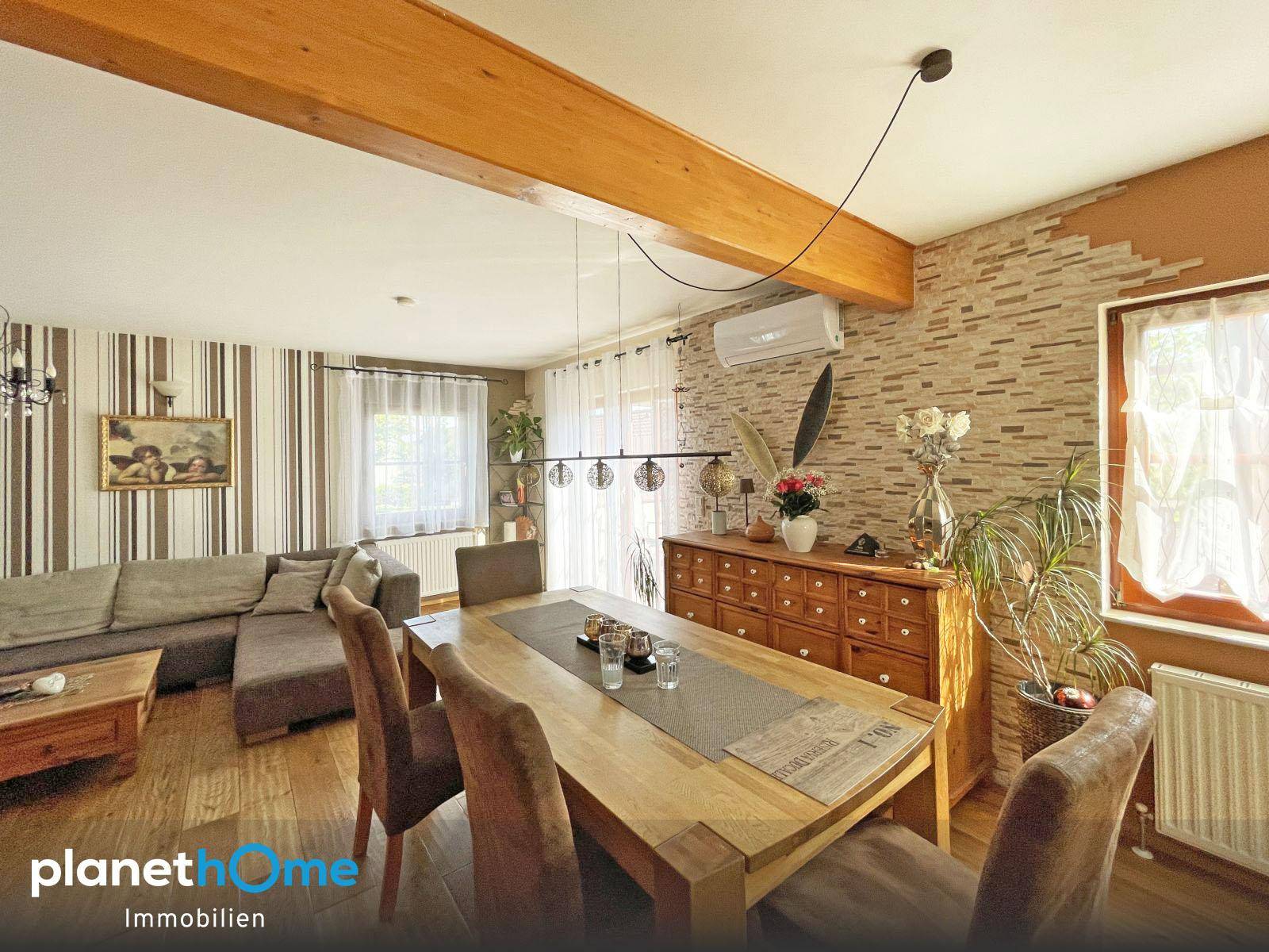 Essbereich mit großem Holztisch, Holzboden und dekorativer Steinwand im offenen Wohnkonzept.