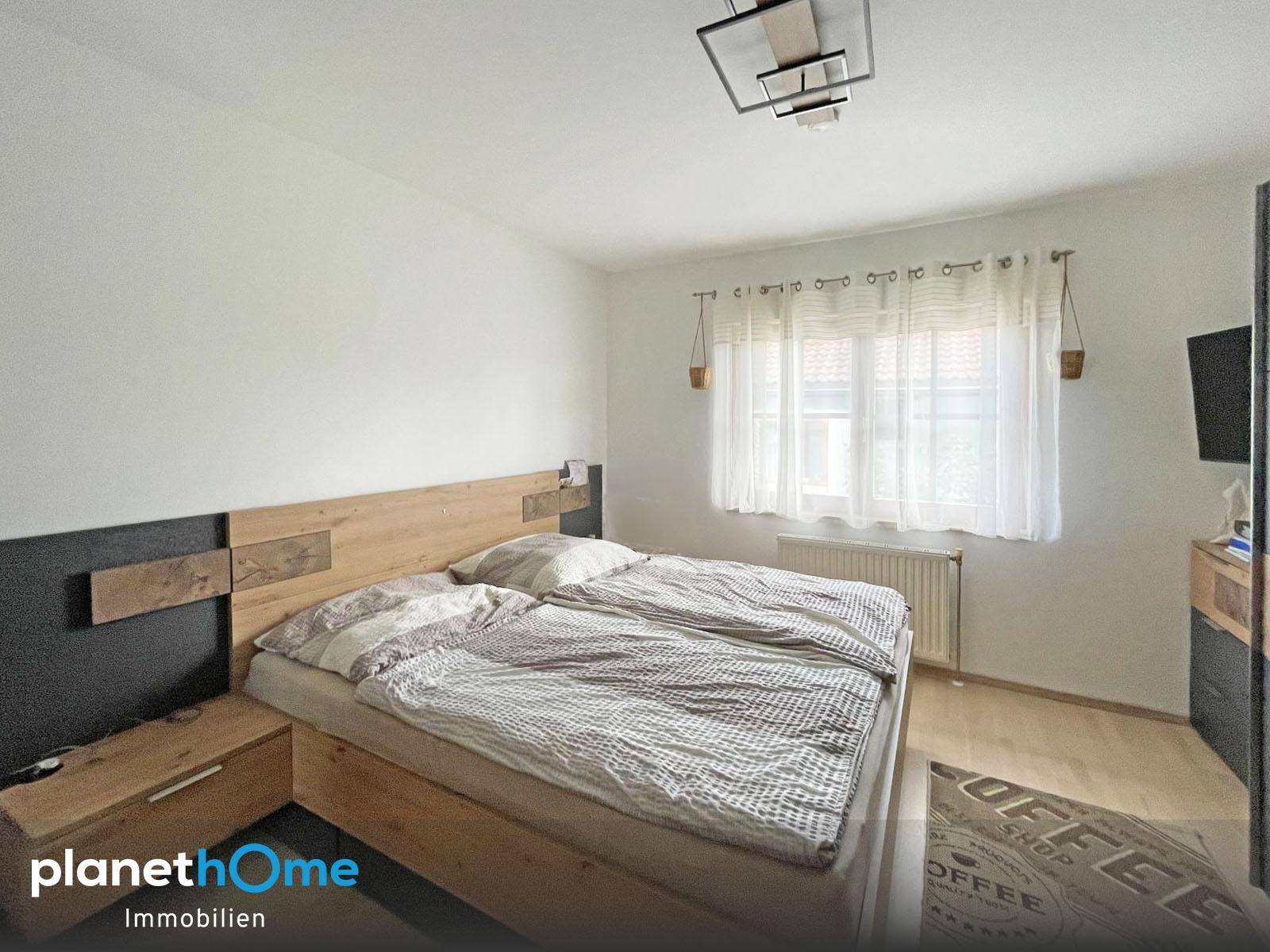 Helles Schlafzimmer mit Doppelbett, Fenster und Laminatboden.