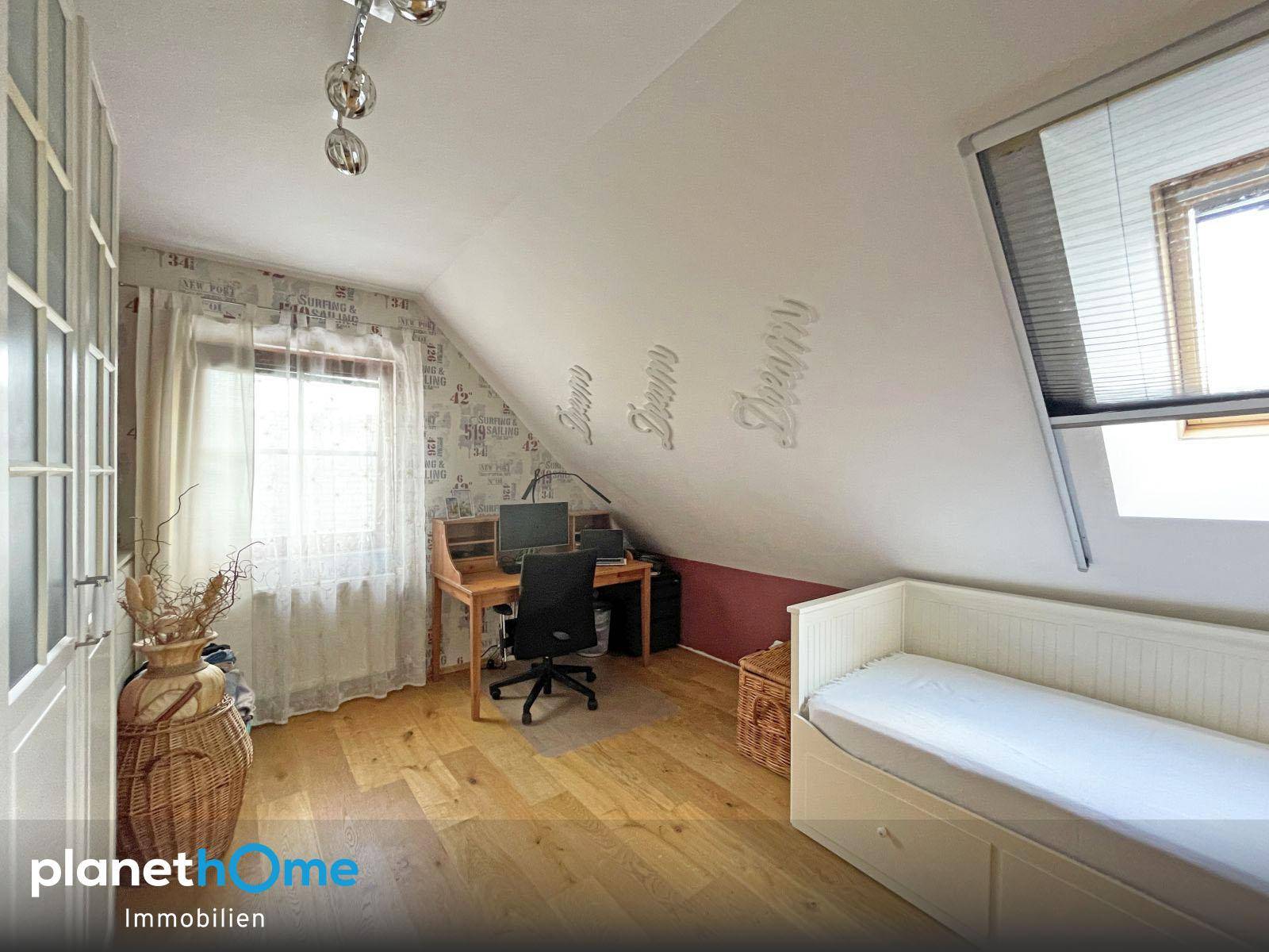 Helles Arbeitszimmer im Dachgeschoss mit Schreibtisch, Bett und Holzboden.