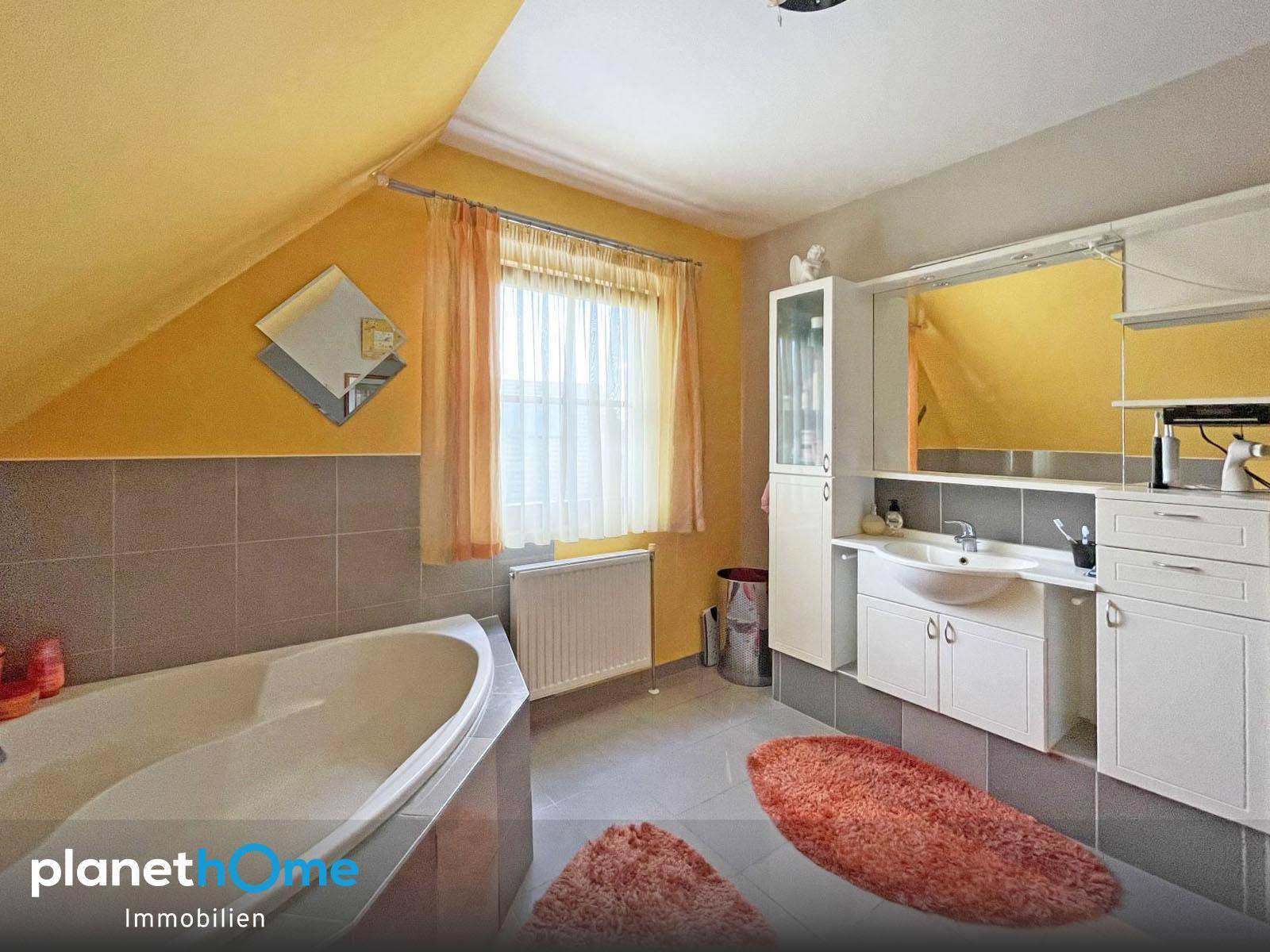Badezimmer im Dachgeschoss mit Badewanne, Waschbecken und gelben Wänden.