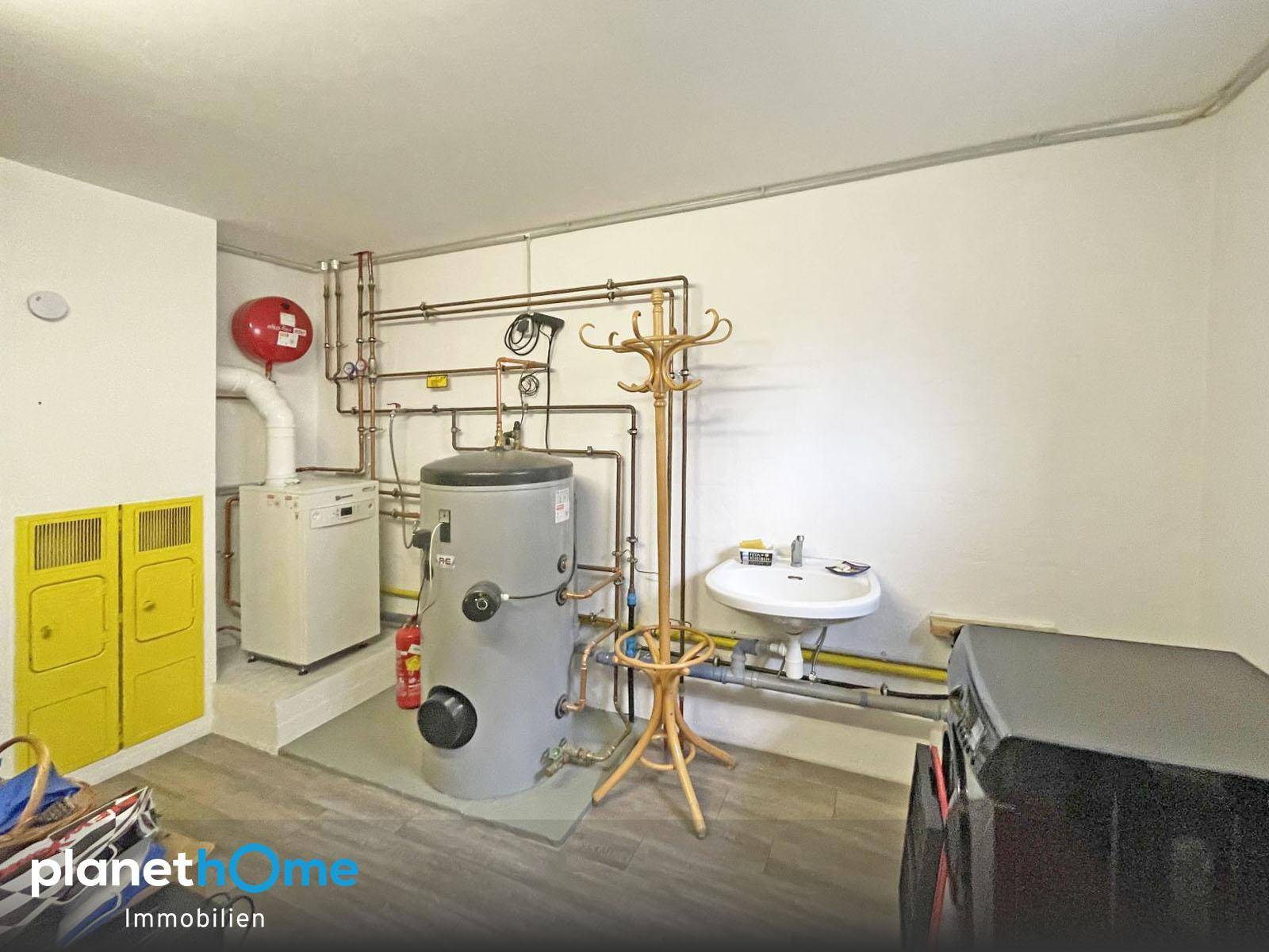 Hauswirtschaftsraum mit Warmwasserboiler, Heizungsinstallationen und kleinem Waschbecken.