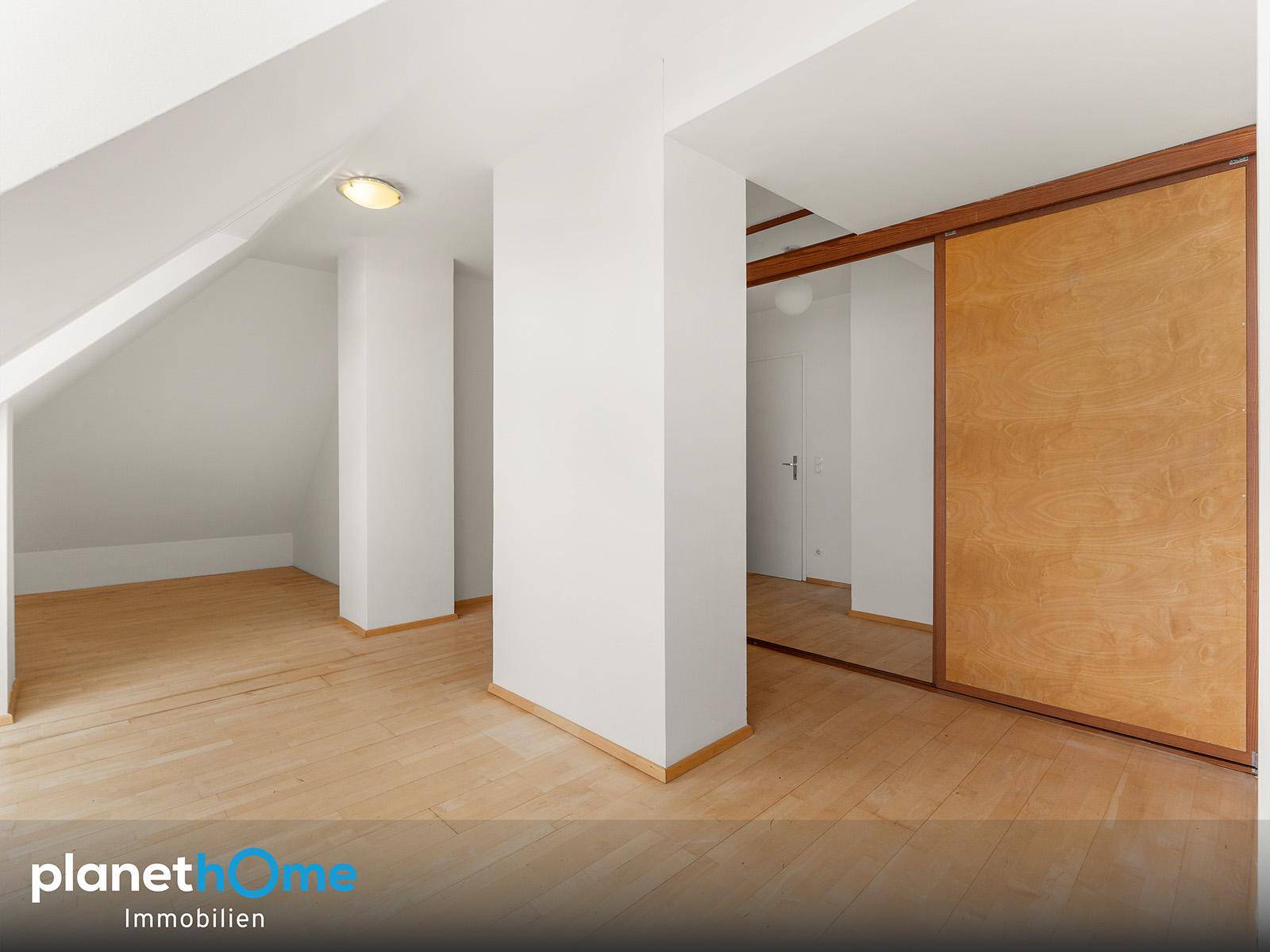 Geräumiger Raum mit Holzboden, Dachschräge und großem Einbauschrank mit Schiebetüren.