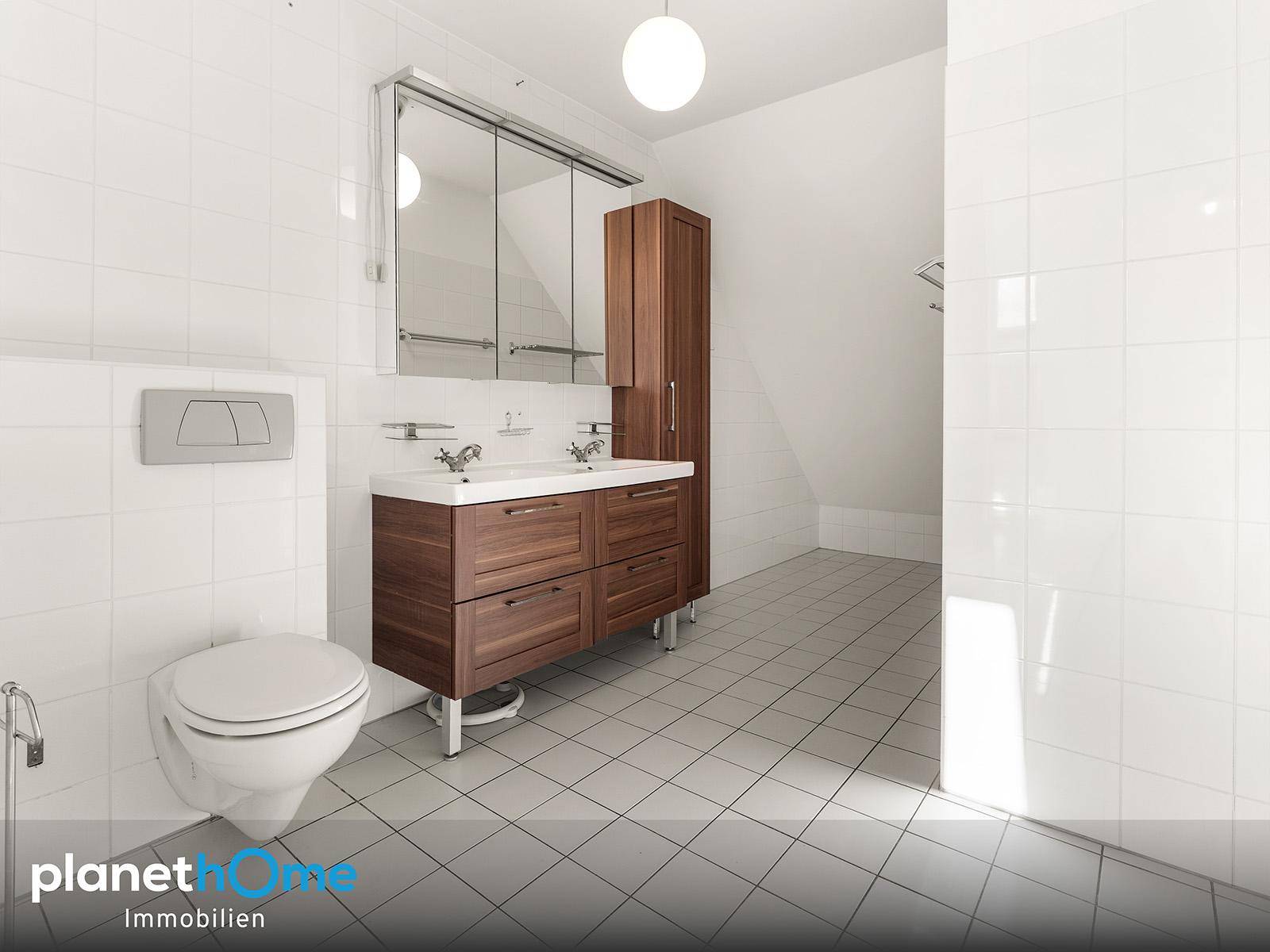Helles Badezimmer mit weißen Fliesen, Doppelwaschbecken und Spiegelschrank.