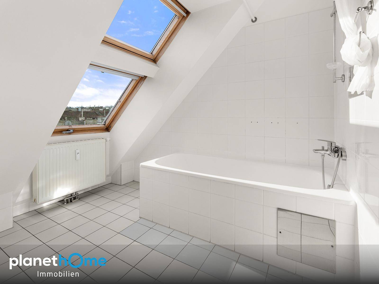 Helles Badezimmer mit Badewanne, weißen Fliesen und zwei Dachfenstern in der Dachschräge.