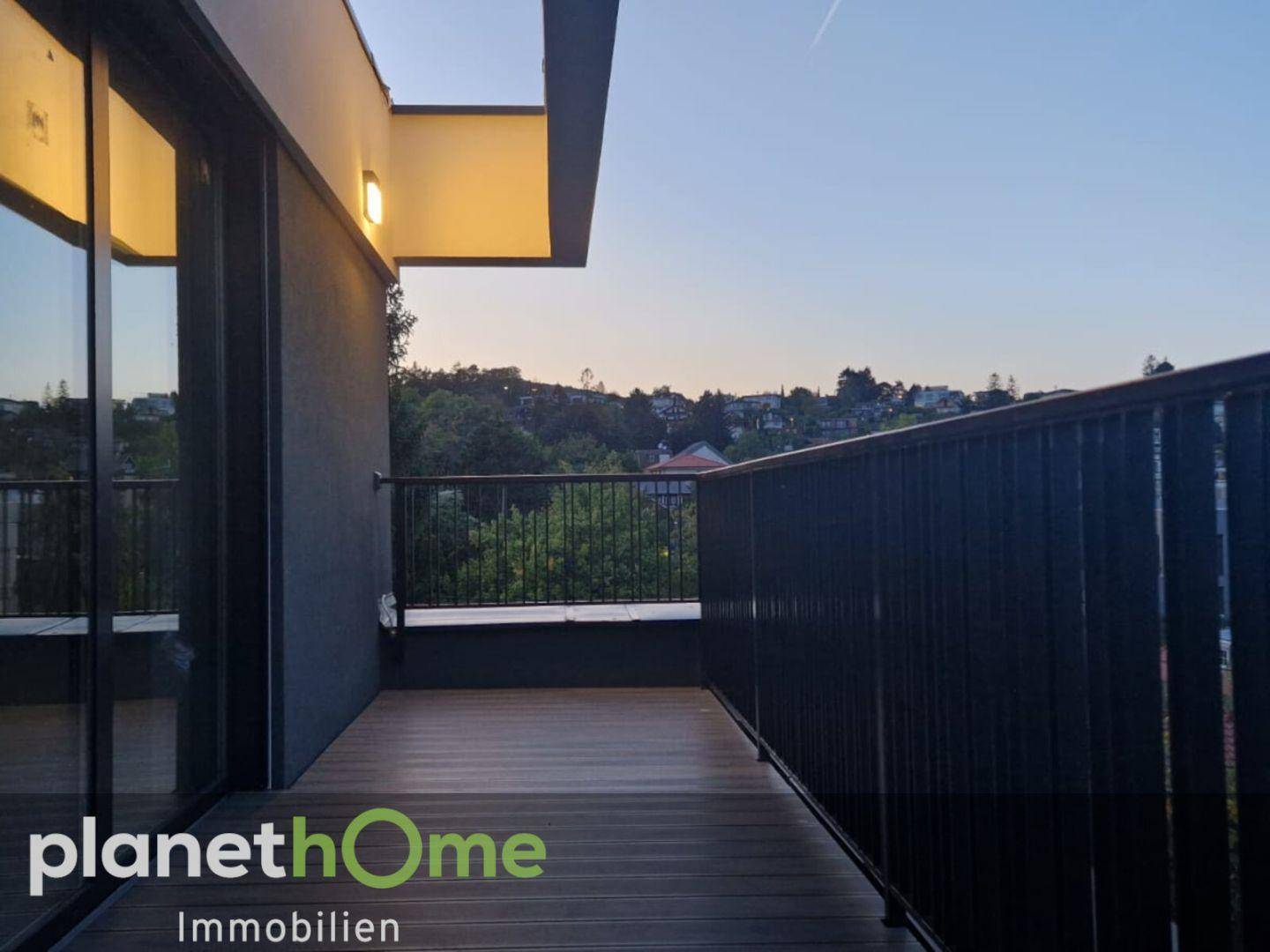 Balkon am Abend mit Holzboden und Blick auf die grüne, hügelige Umgebung.