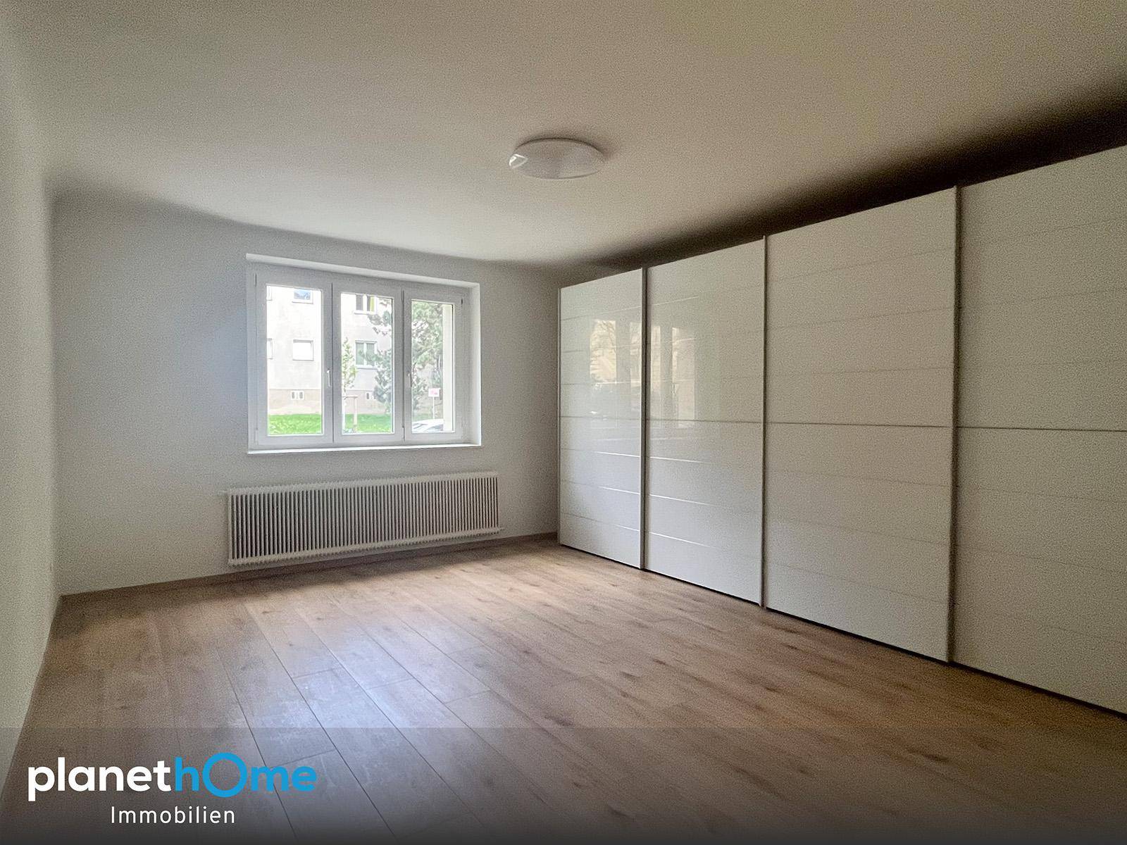 Helles Schlafzimmer mit Holzboden und großen weißen Einbauschränken entlang einer Wand.