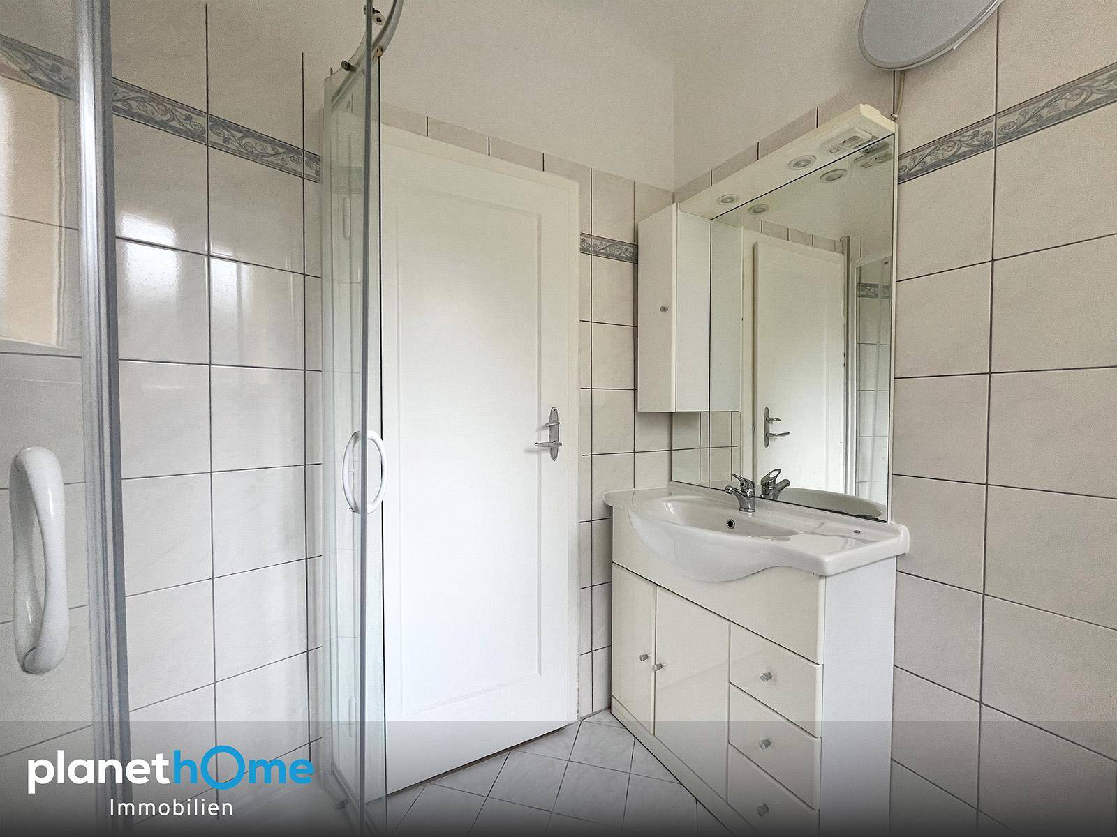 Älteres Badezimmer mit weißen Fliesen, Duschkabine und Waschbecken mit Spiegelschrank.