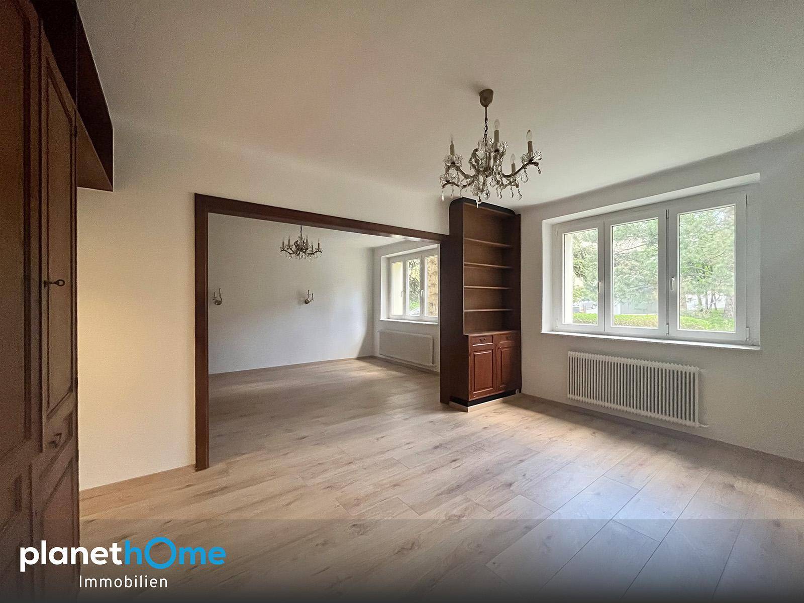 Geräumiges, unmöbliertes Wohnzimmer mit Holzboden und integriertem Regal sowie Durchgang zu weiterem Raum.